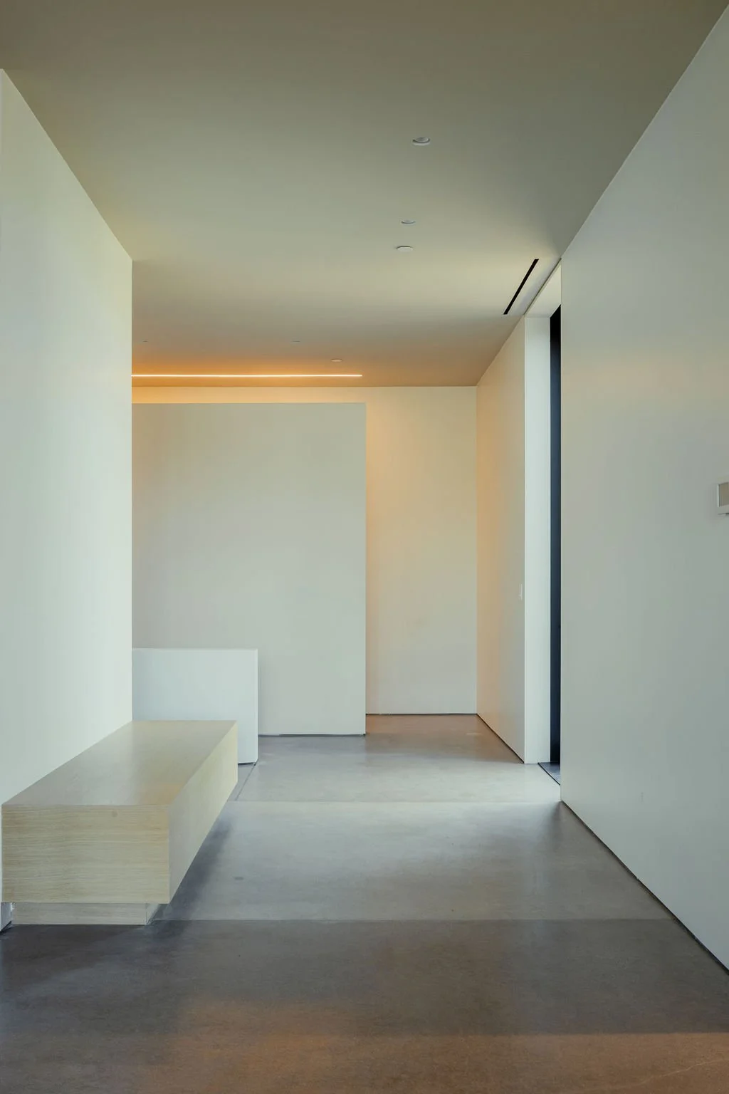 Minimalist interior with light-colored walls, a bench, and a sliding door, illuminated by soft lighting.