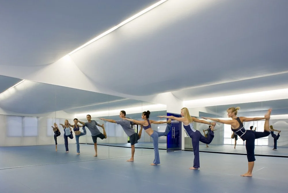 Group of people practicing yoga in a studio with mirrors, performing balancing poses.