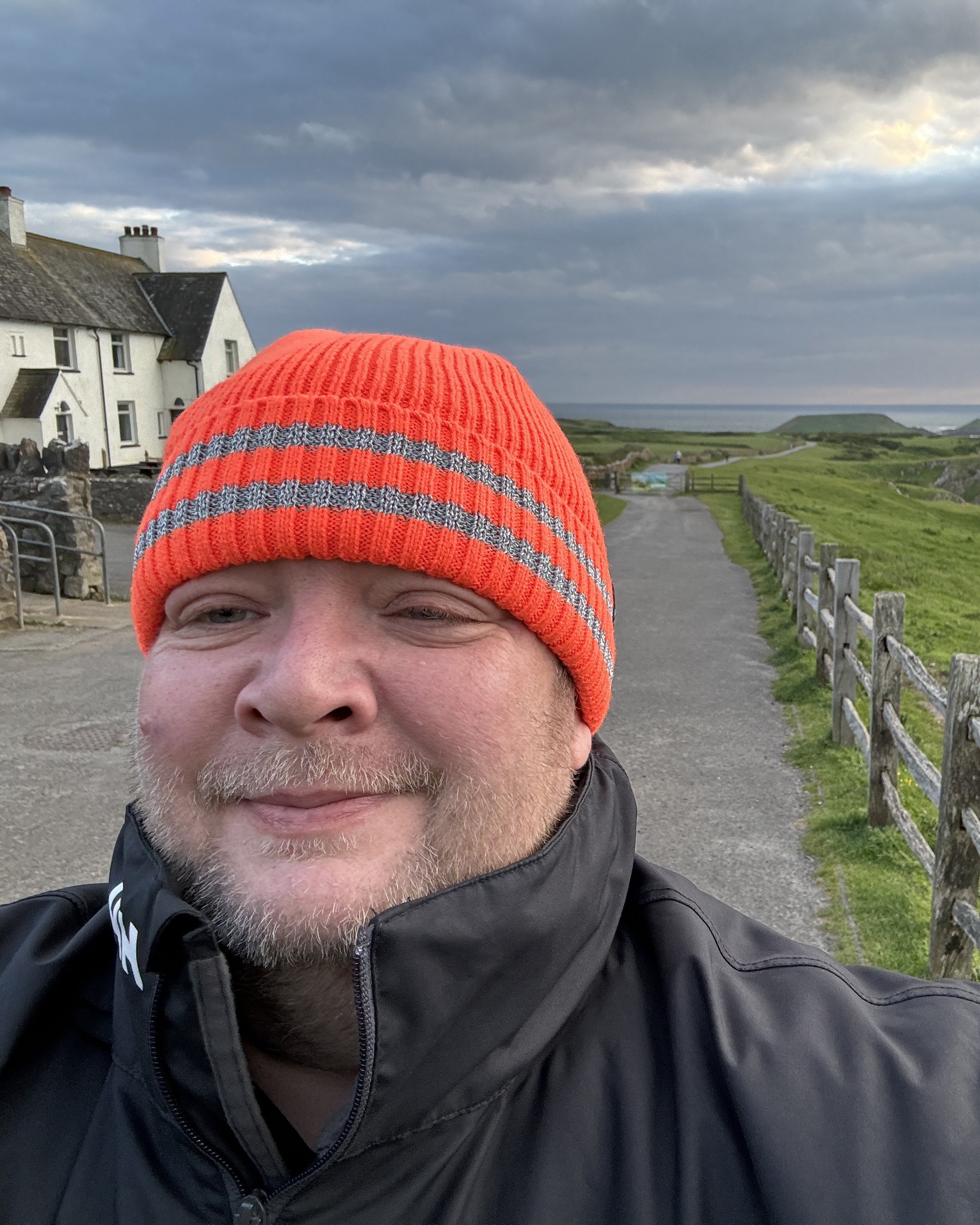 Head shot of Gavin the owner of Ruff Draft and photographer in Rhossili, Gower, South Wales standing on a footpath heading towards Wormshead in the distance.