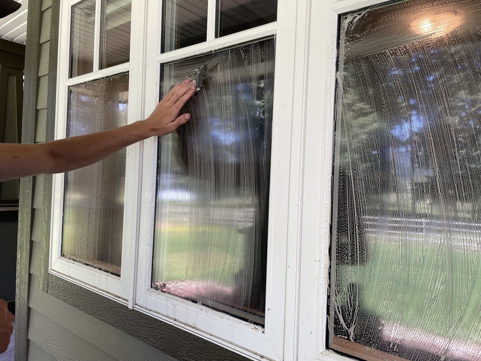 Person cleaning the outside of a window with soapy water, soap suds visible on the glass