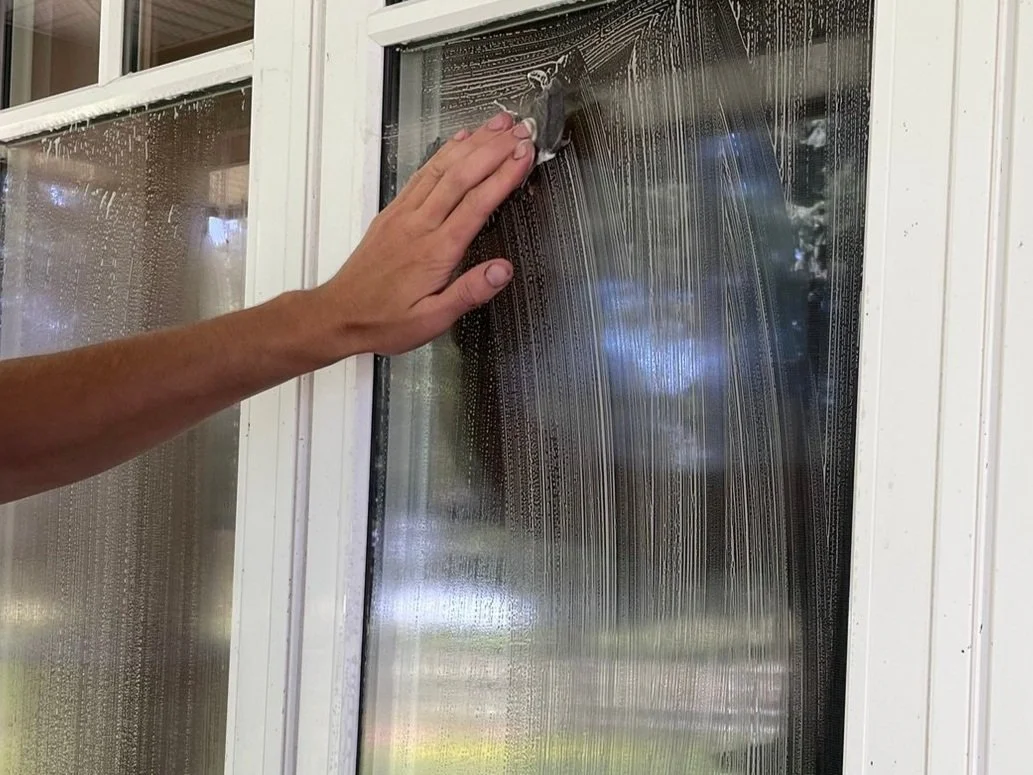 Person cleaning a glass window with a cloth, leaving a soapy streak.