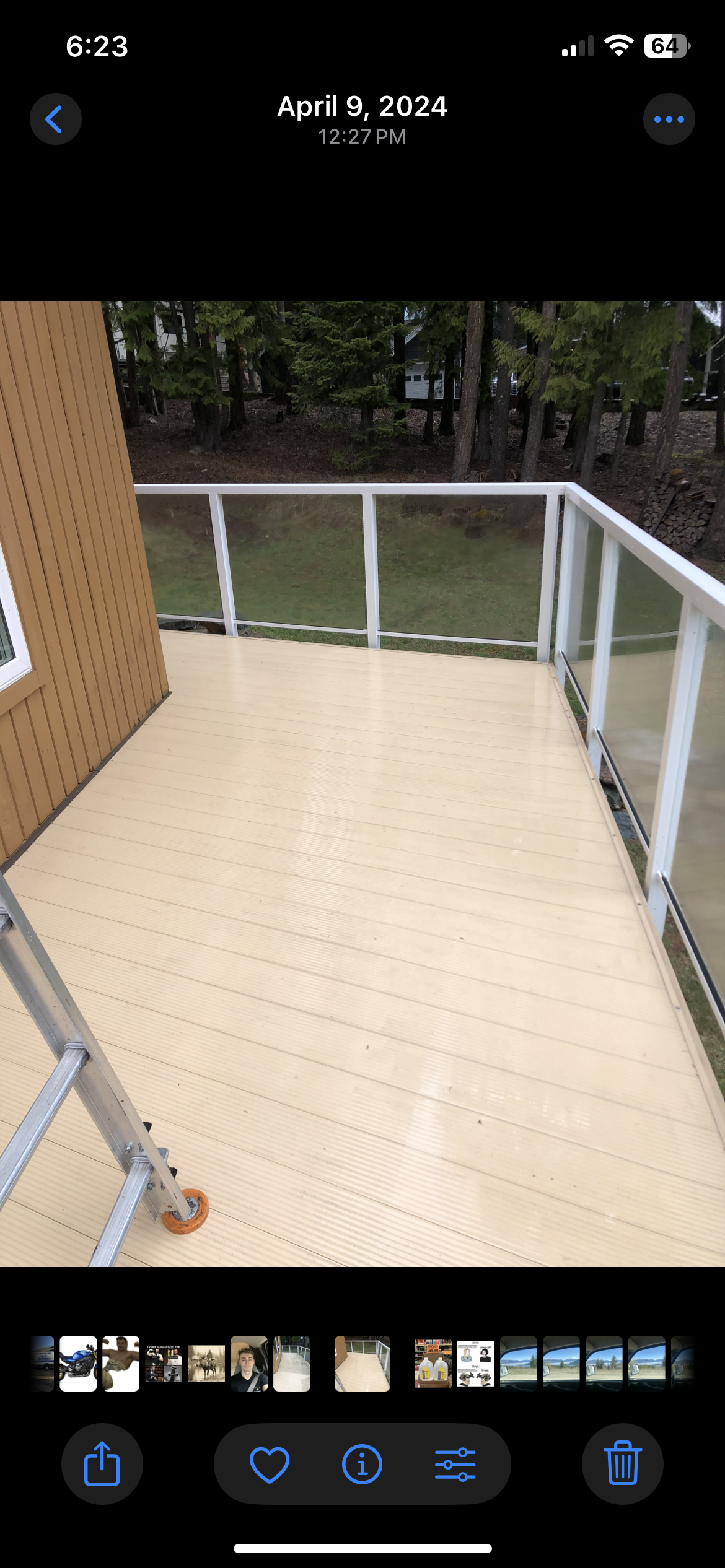 Newly constructed wooden balcony with white railing, part of a house with wood siding, overlooking a backyard with grass and trees.