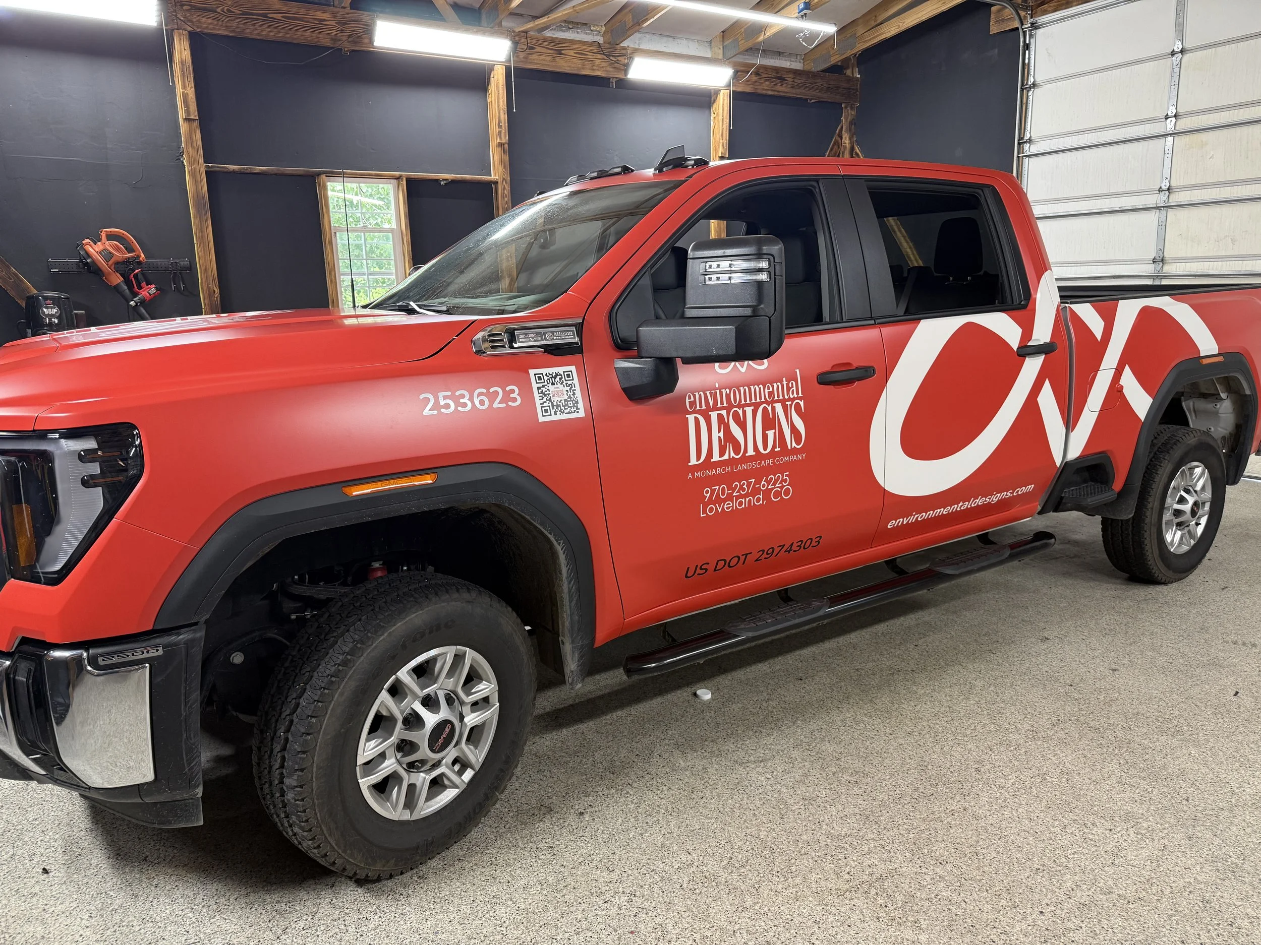 Red pickup truck with environmental designs branding parked inside a garage with black walls and wooden accents.