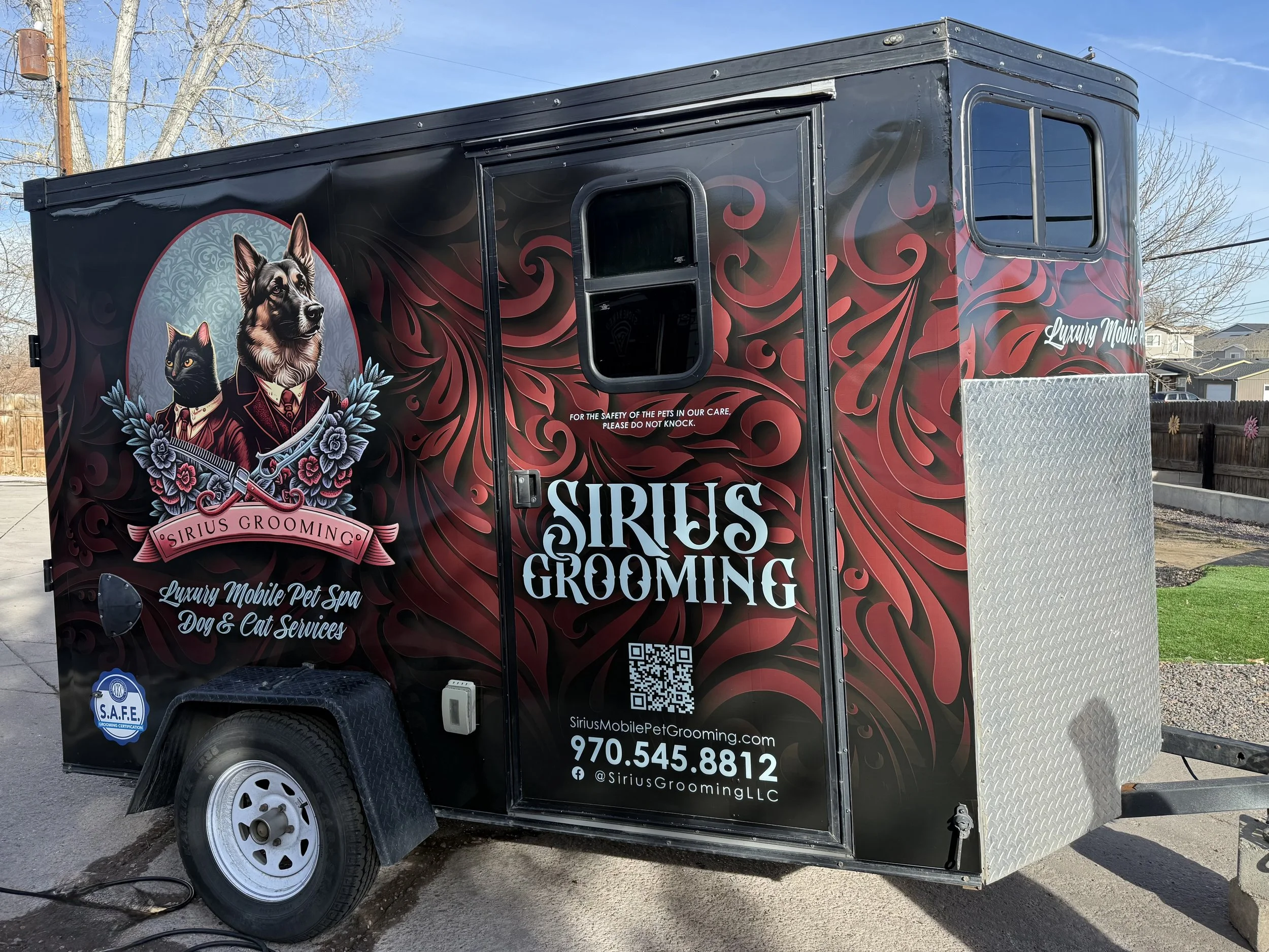 A black mobile pet grooming trailer with decorative artwork and animals on the side, including a dog and a cat, and the text "Luxury Mobile Pet Spa Dog & Cat Services."