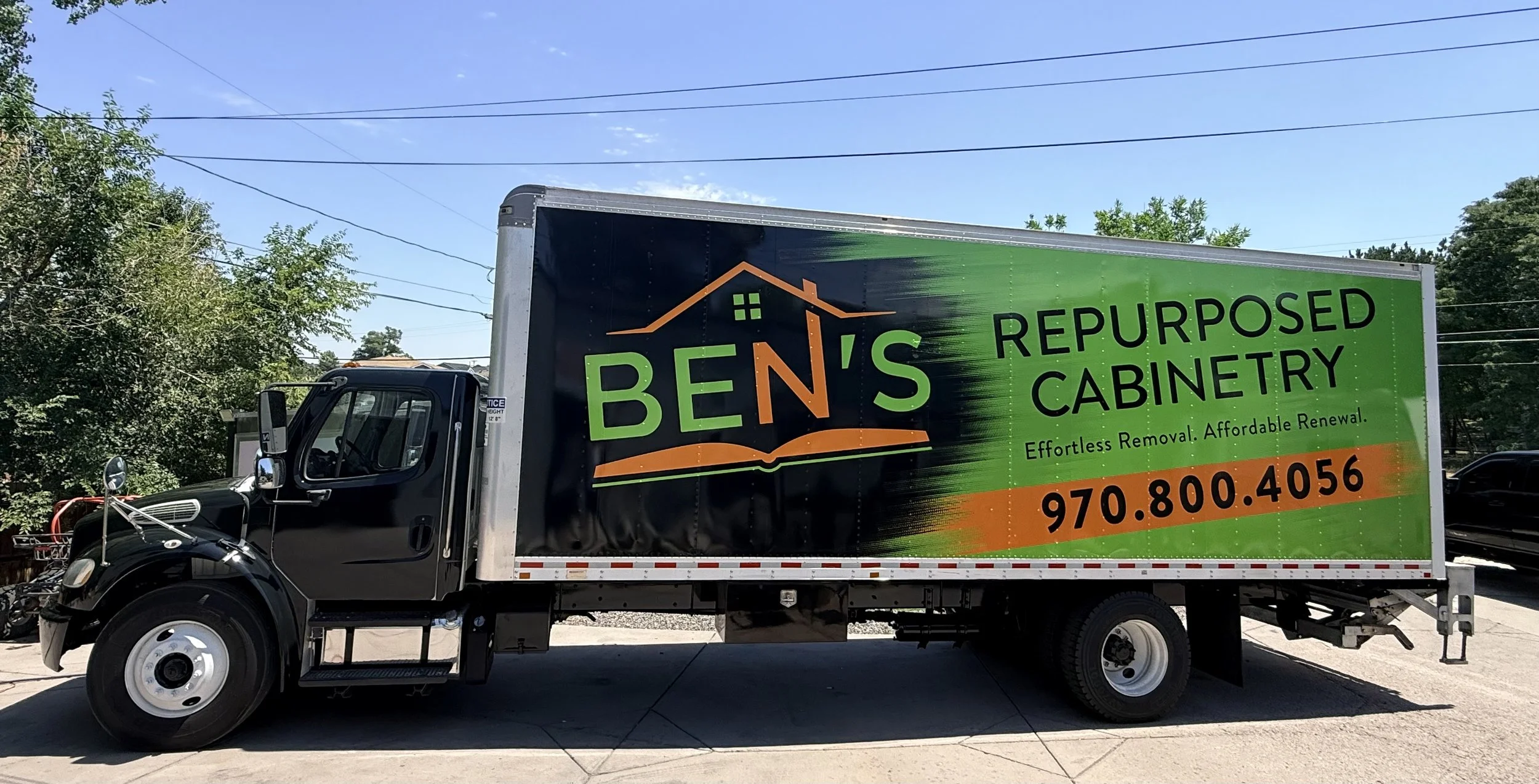 A truck with a green and black advertisement for BENS Repurposed Cabinetry, offering effortless removal and affordable renewal, includes a phone number 970-800-4056.
