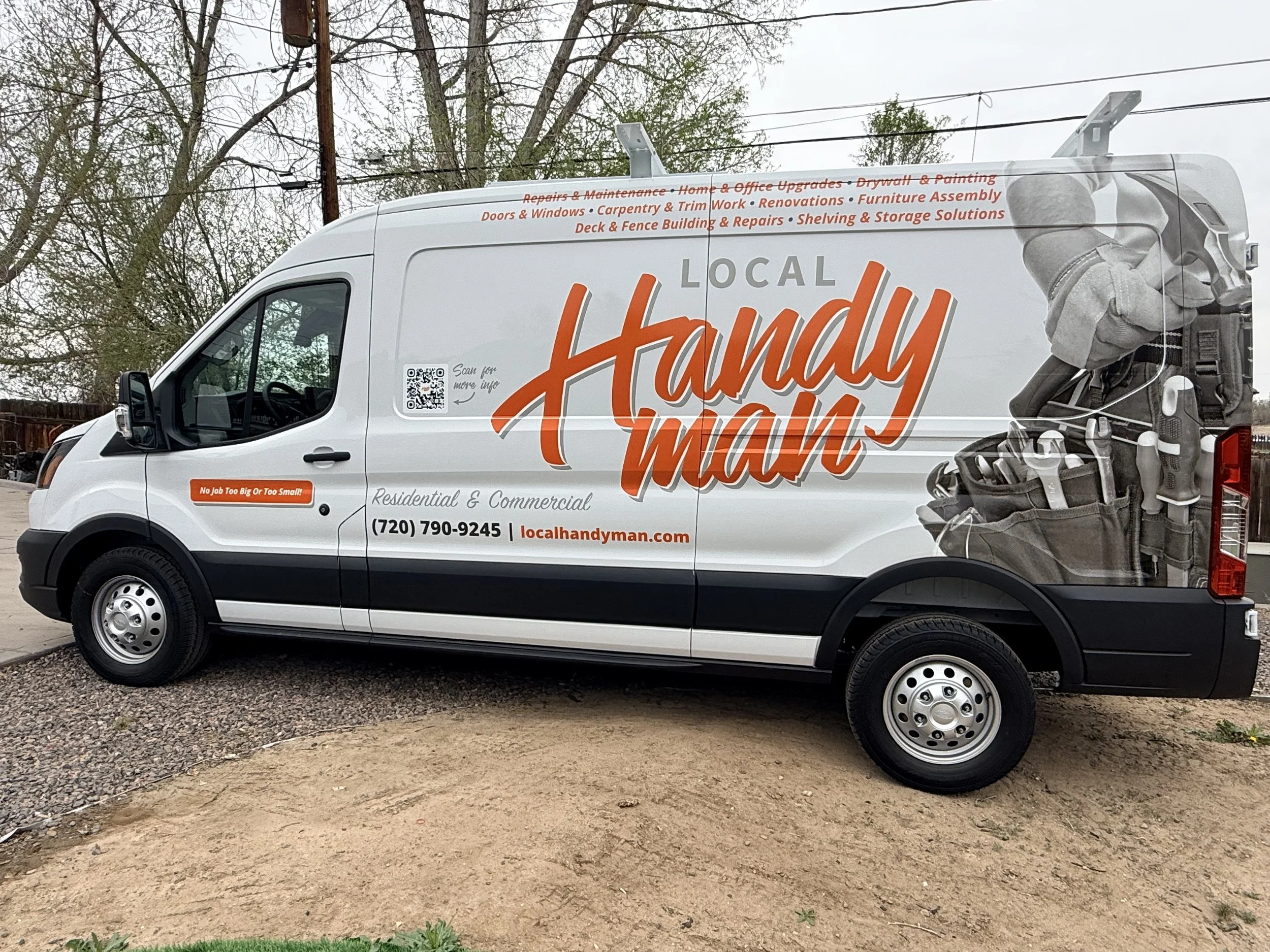 White handyman service van parked on a dirt lot with trees and power lines in the background. The van features branding for local handyman services, including a large logo and list of services such as repairs, remodeling, and carpentry.