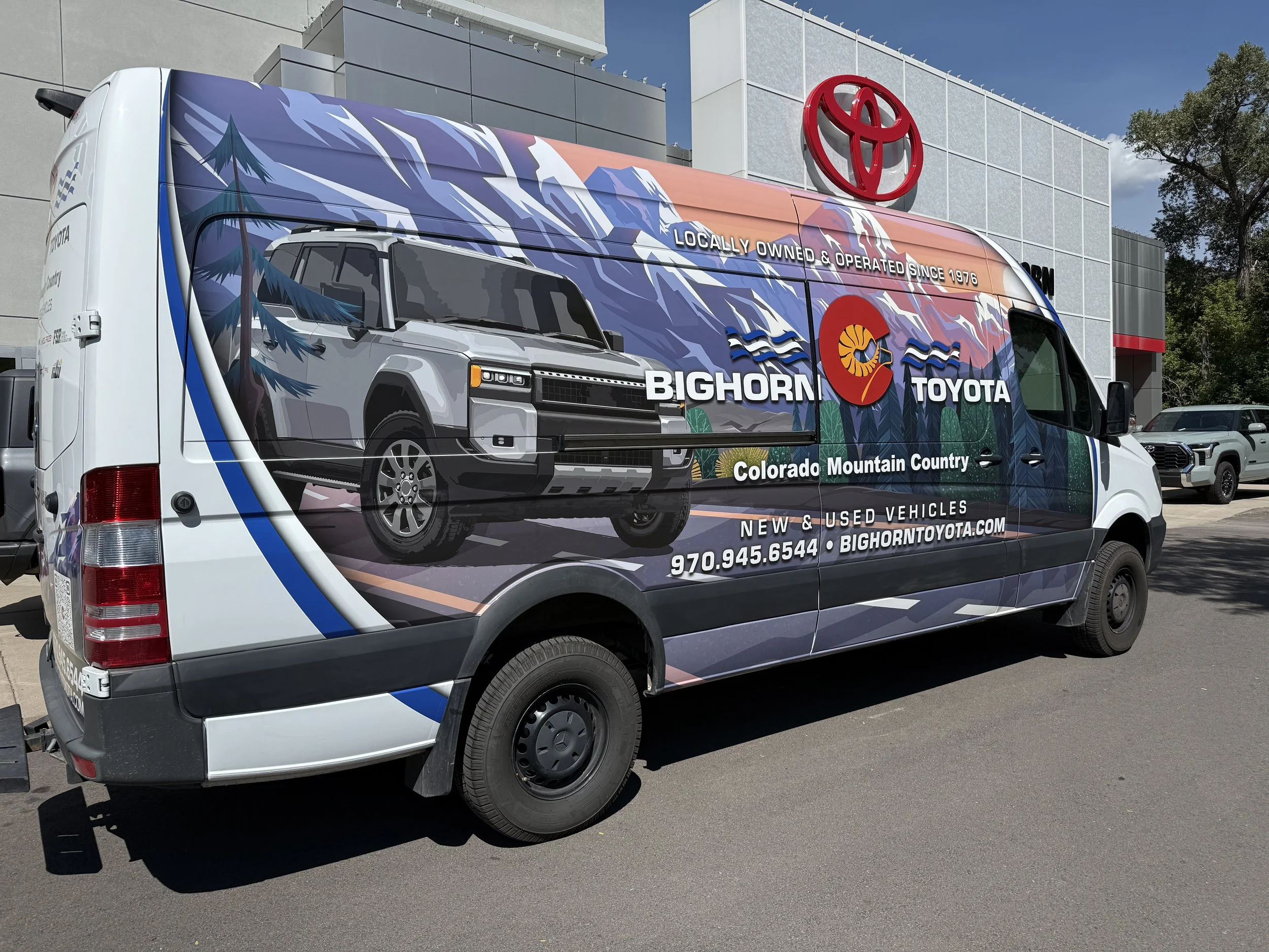 A delivery van parked outside a Toyota dealership, featuring a mountain landscape with trees and the text 'Locally Owned & Operated Since 1976' and 'Big Horn Toyota' branding.