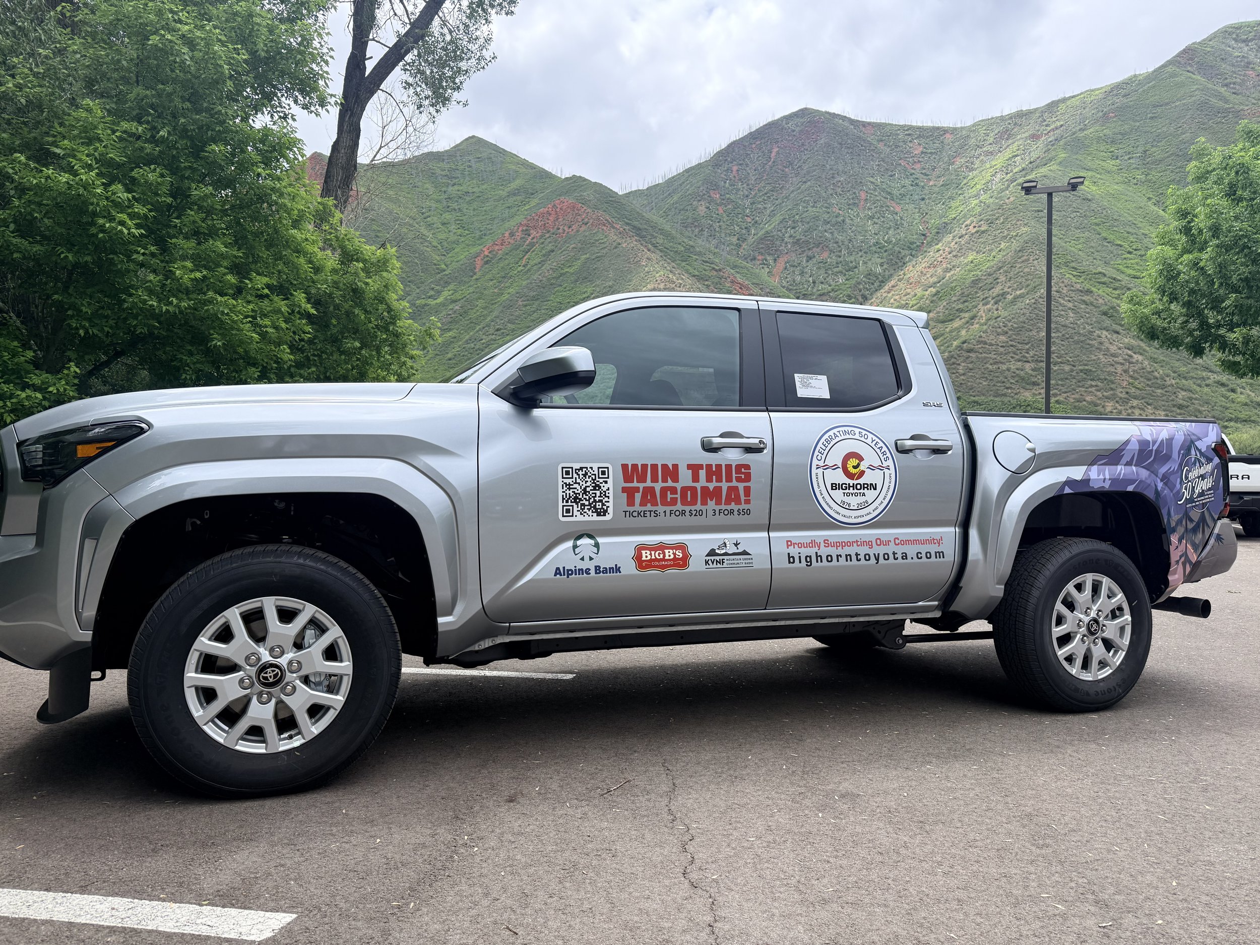 A silver pickup truck parked in a parking lot with green mountains and cloudy sky in the background.
