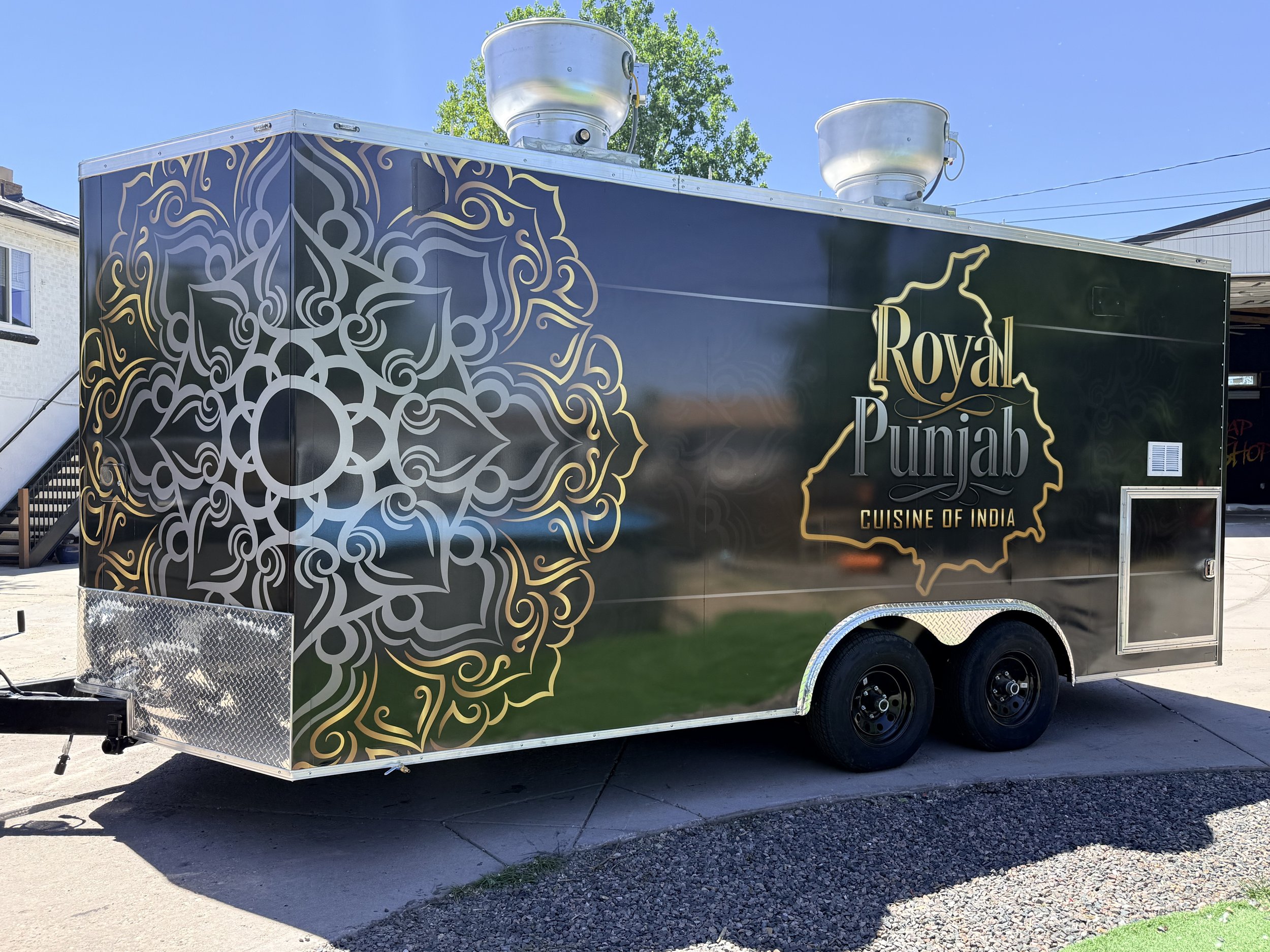 A food truck with a black exterior, decorated with an intricate gold and white pattern and the words "Royal Punjab Cuisine of India."