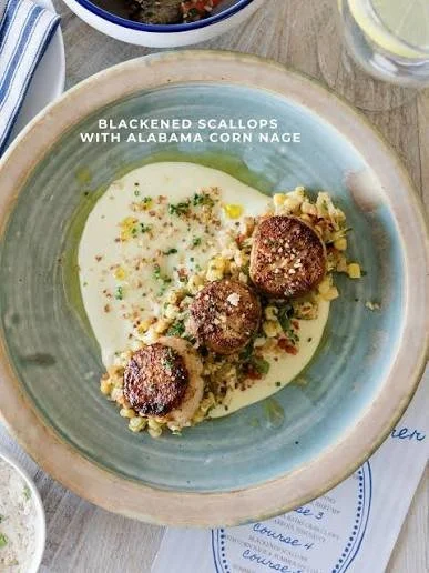 Blackened scallops with Alabama corn nage on a ceramic plate, garnished with herbs and served with a creamy sauce.