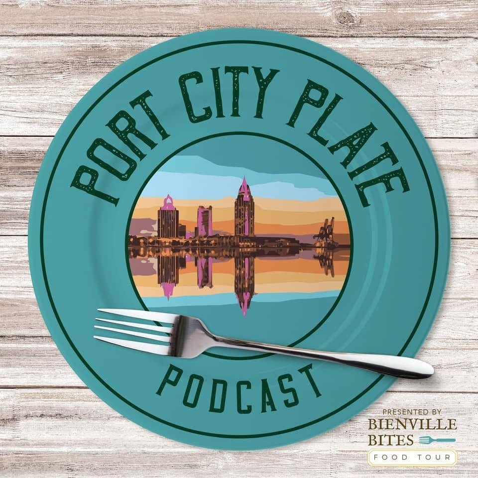 A circular podcast logo with the text 'Port City Place Podcast' around the edge. The center features an illustration of a city skyline with tall buildings reflecting on water, under a colorful sky. A fork lies across the bottom of the circle.