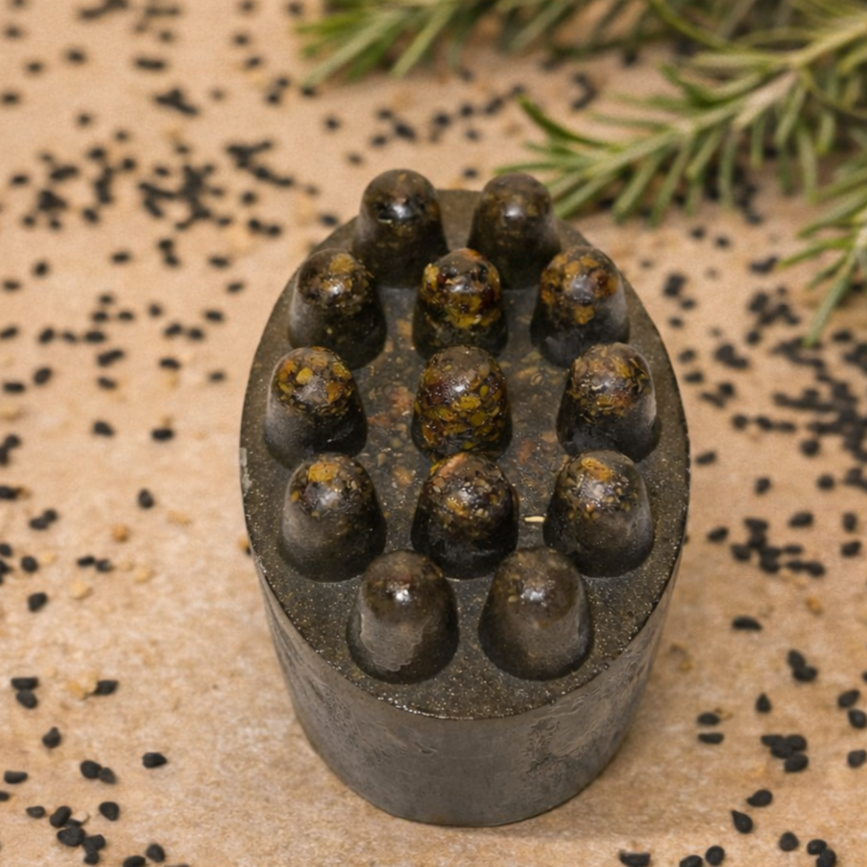 Black soap with small fenugreek seeds, surrounded by black seeds and rosemary on a brown surface.