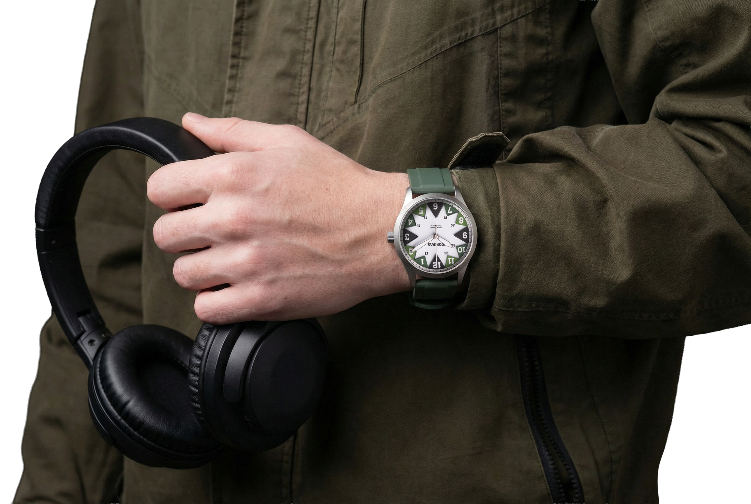 Person wearing a green watch on their wrist, holding black headphones, and wearing an olive green jacket.