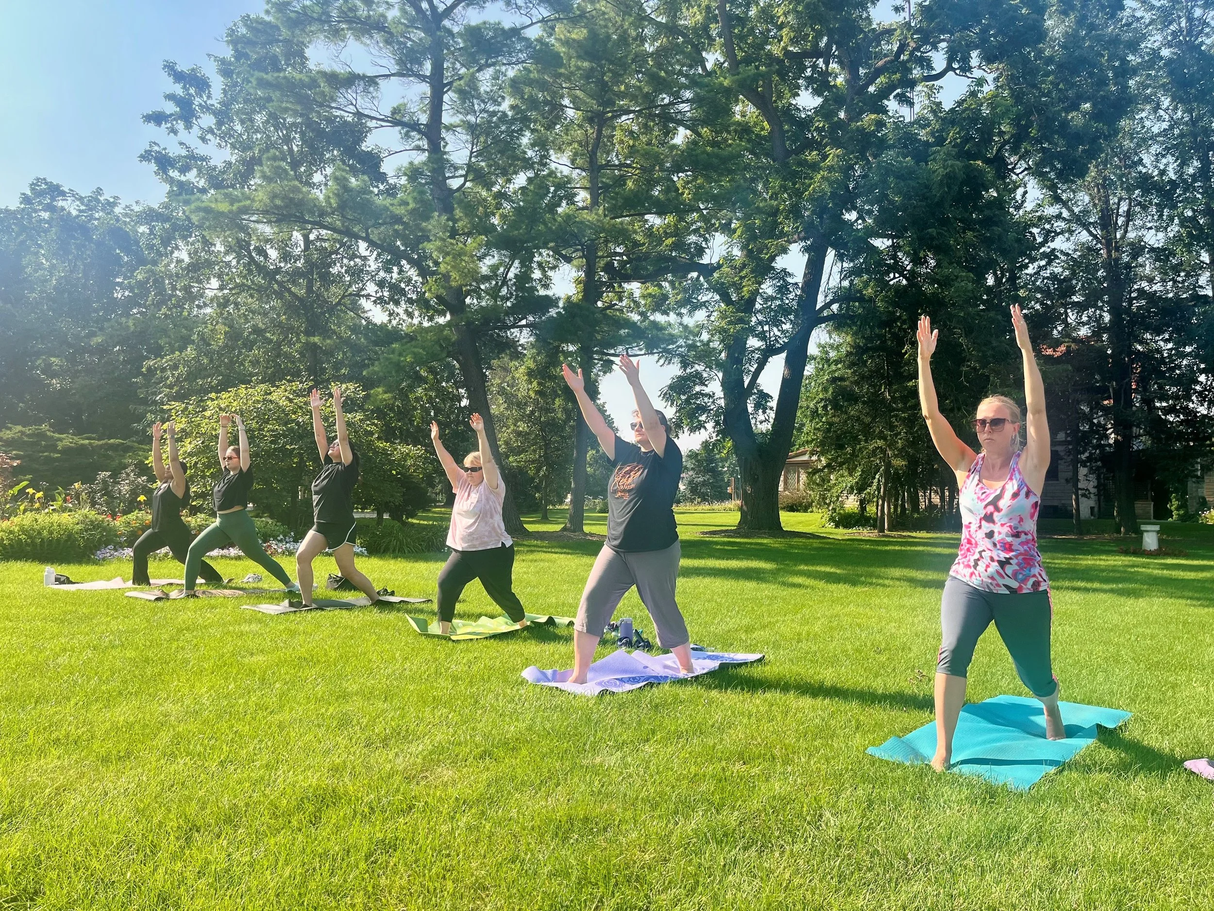 A group of people doing yoga in a grassy yard on a sunny day