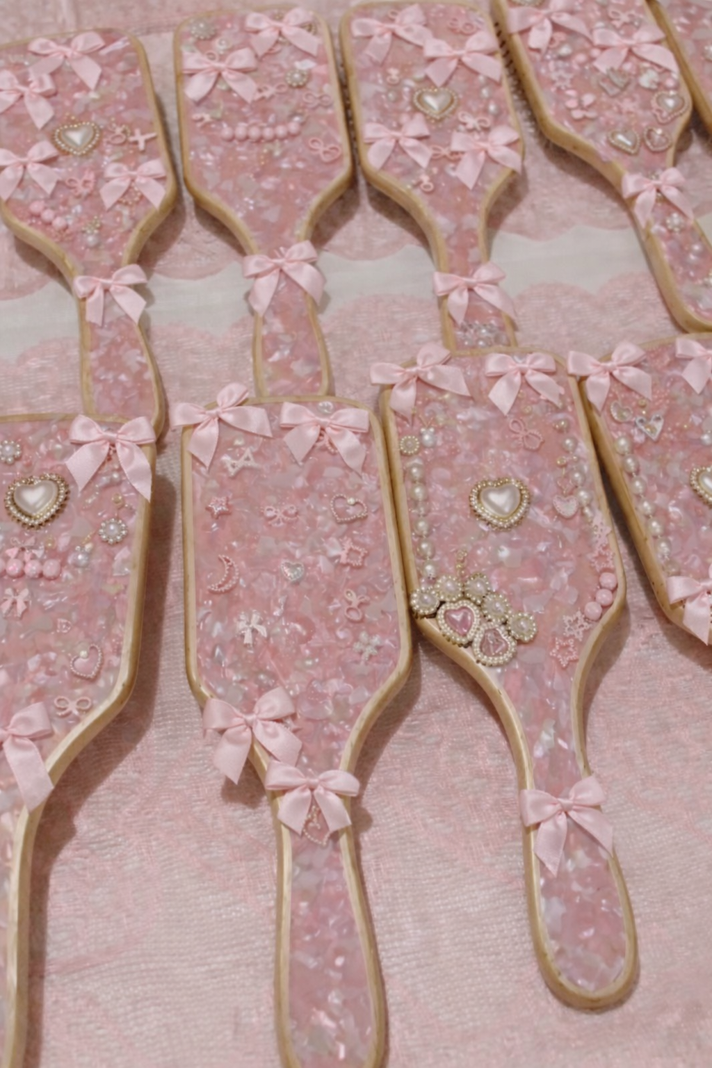 Custom pink marbled hairbrushes adorned with satin bows, pearl embellishments, and charms. These personalized brushes are featured in Blush & Bliss by Mya’s interactive entertainment experiences for kids’ birthday parties, teen birthday parties, bat 