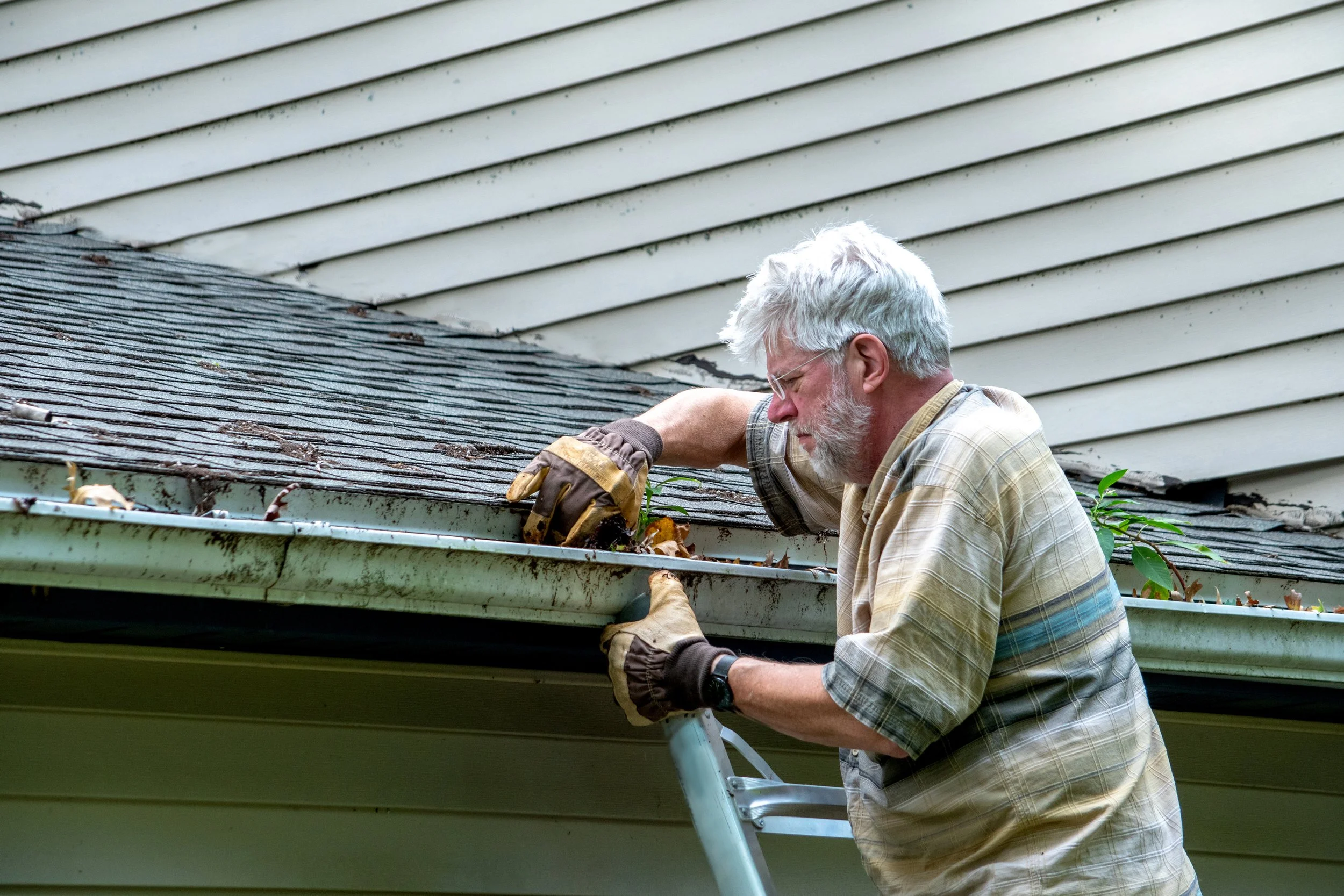 Homeowner cleaning debris from gutters during spring maintenance to prevent water damage
