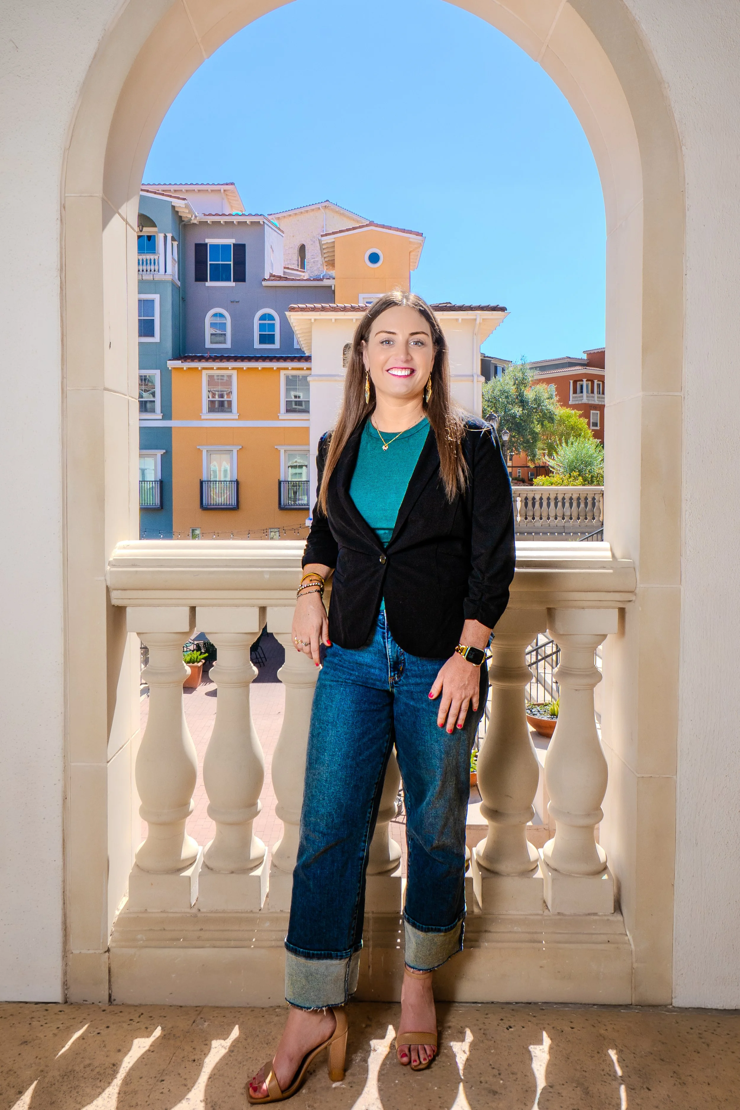 A woman standing on a balcony with colorful apartment buildings in the background on a sunny day.