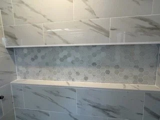 Close-up of tiled bathroom wall with large marble-like tiles and a decorative mosaic strip.