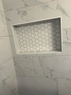 Built-in wall shower niche with hexagonal tile background inside a tiled bathroom wall.