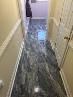 A hallway with marble flooring, yellow walls with white trim, a closed white door on the right, and a purple wall at the end with a window.