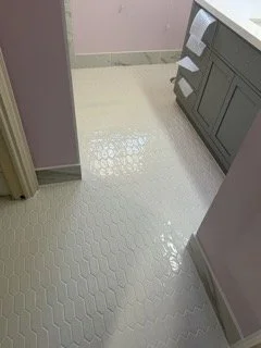Shiny white hexagonal tile floor in a kitchen or laundry room with gray cabinets and pink walls.