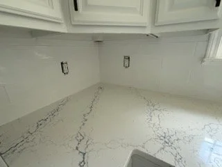 Empty kitchen with white cabinets, marble countertop, and a window