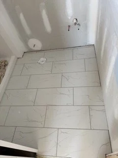Empty corner of a room with white marble floor tiles and unfinished drywall with visible holes.