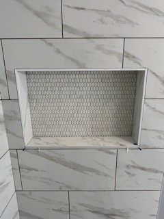 A rectangular wall vent with a honeycomb-patterned cover mounted on a white tiled wall.