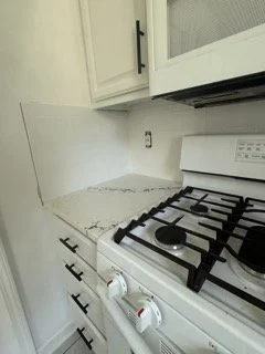 Close-up of a kitchen countertop with a gas stove and white cabinets, with a damaged surface on the counter.