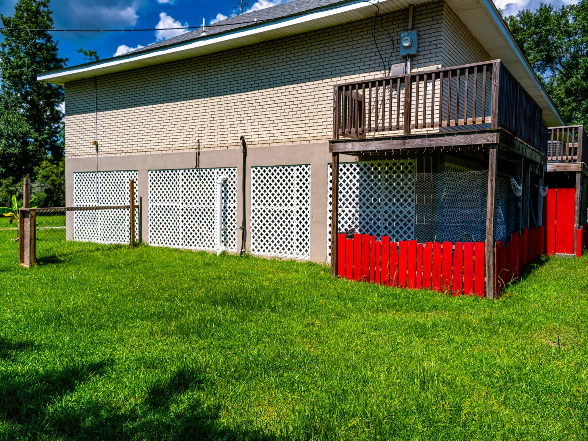 Backyard with a two-story house with brick walls, a wooden deck, and a fenced yard with green grass.