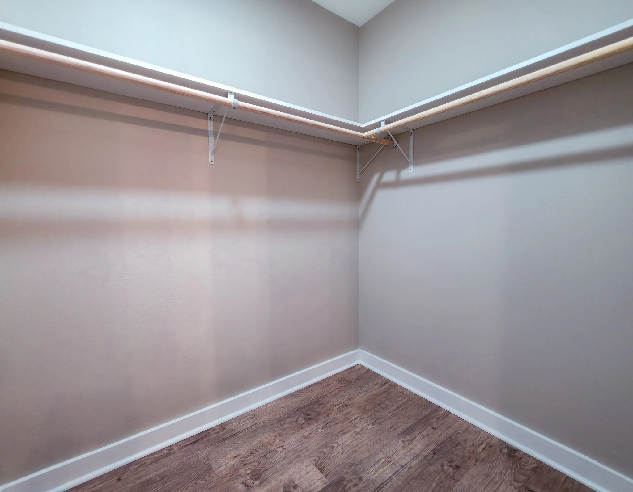 Empty walk-in closet with white shelves and wooden flooring.