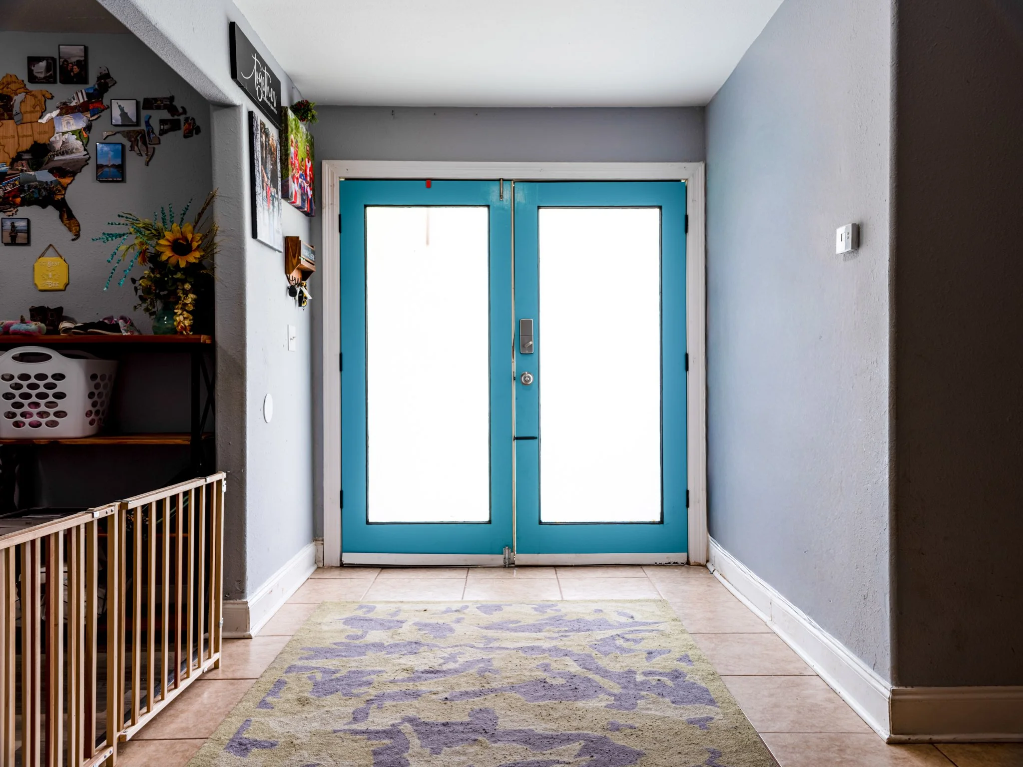 Interior view of a home entryway with closed bright blue door with windows, a colorful rug, wall decorations, and a shelf with various items.