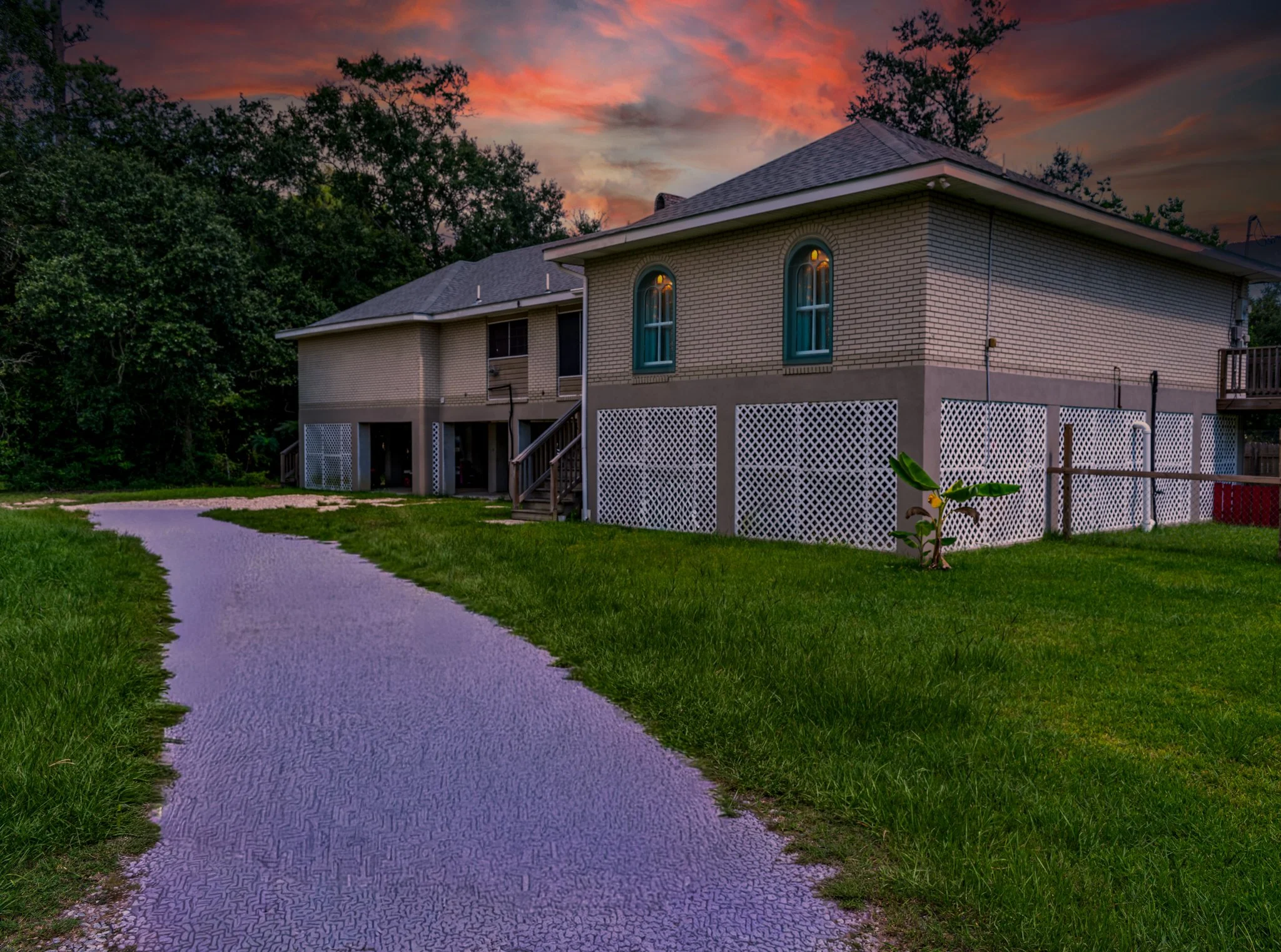 A house with a brick exterior and arched windows, situated on a grassy lawn with a curved driveway, during sunset.