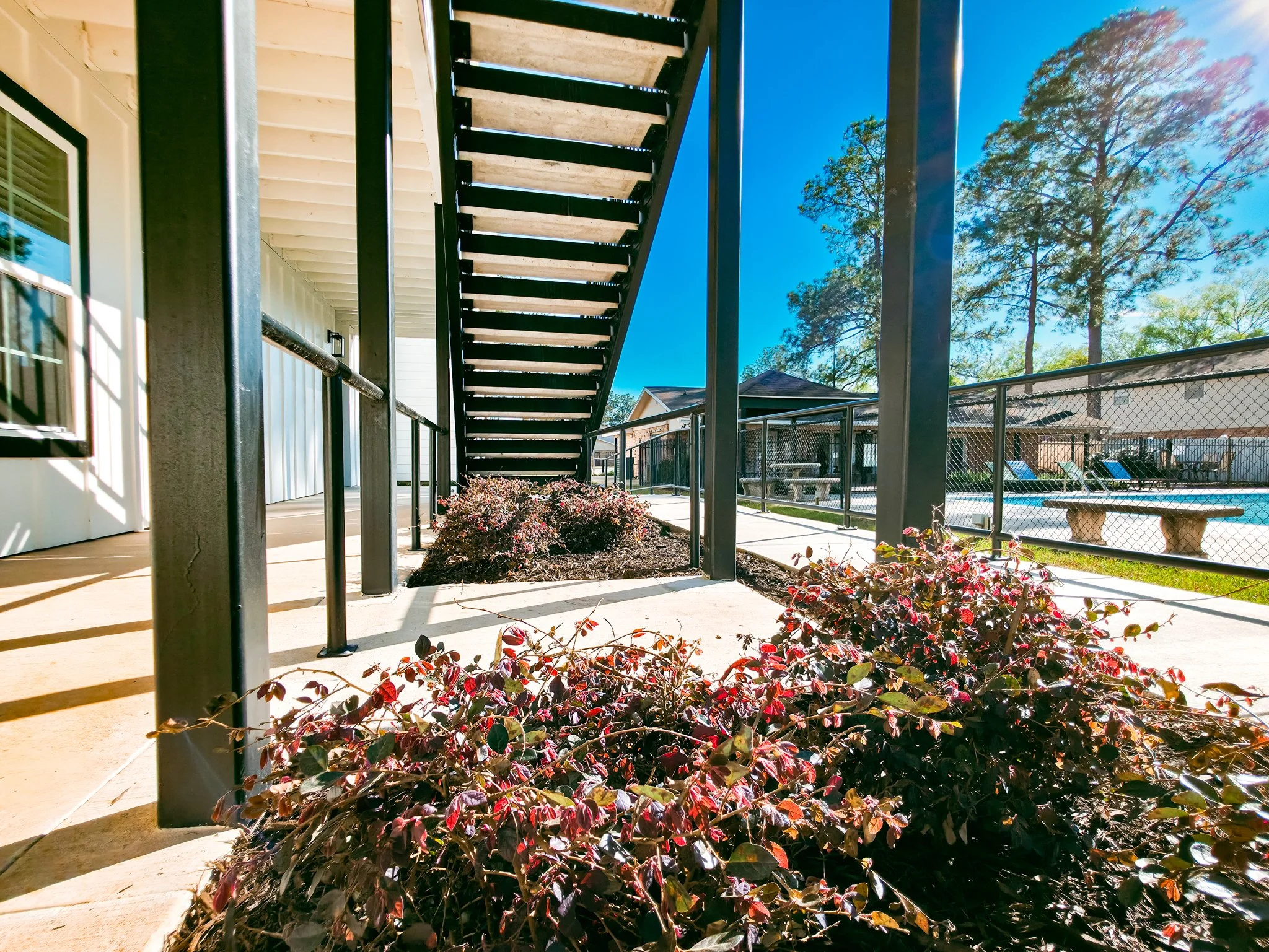 View of outdoor patio with stairs, plants, and swimming pool area under clear blue sky.