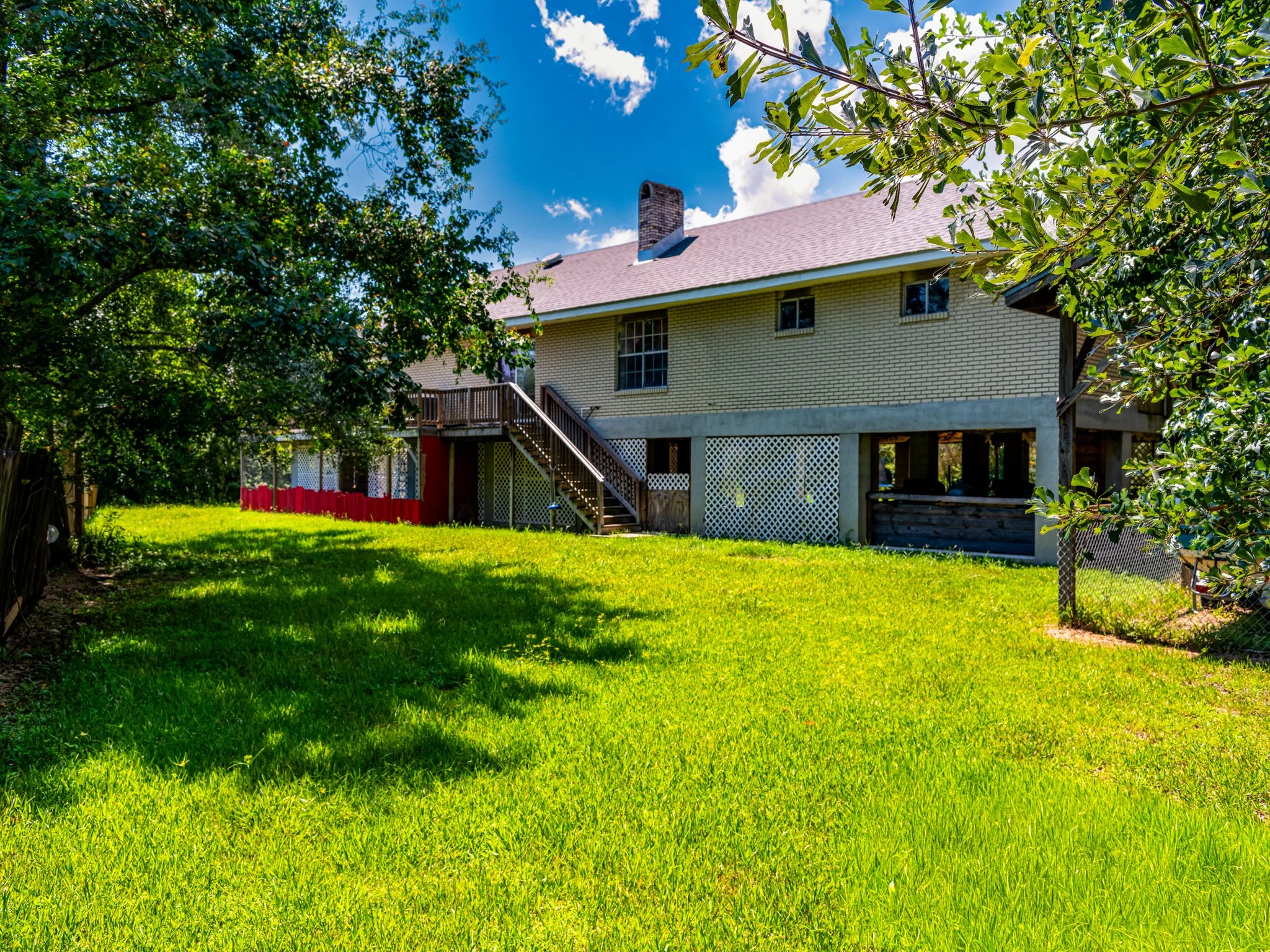 Backyard of a house with green lawn, trees, and a two-story brick house with a balcony and stairs.