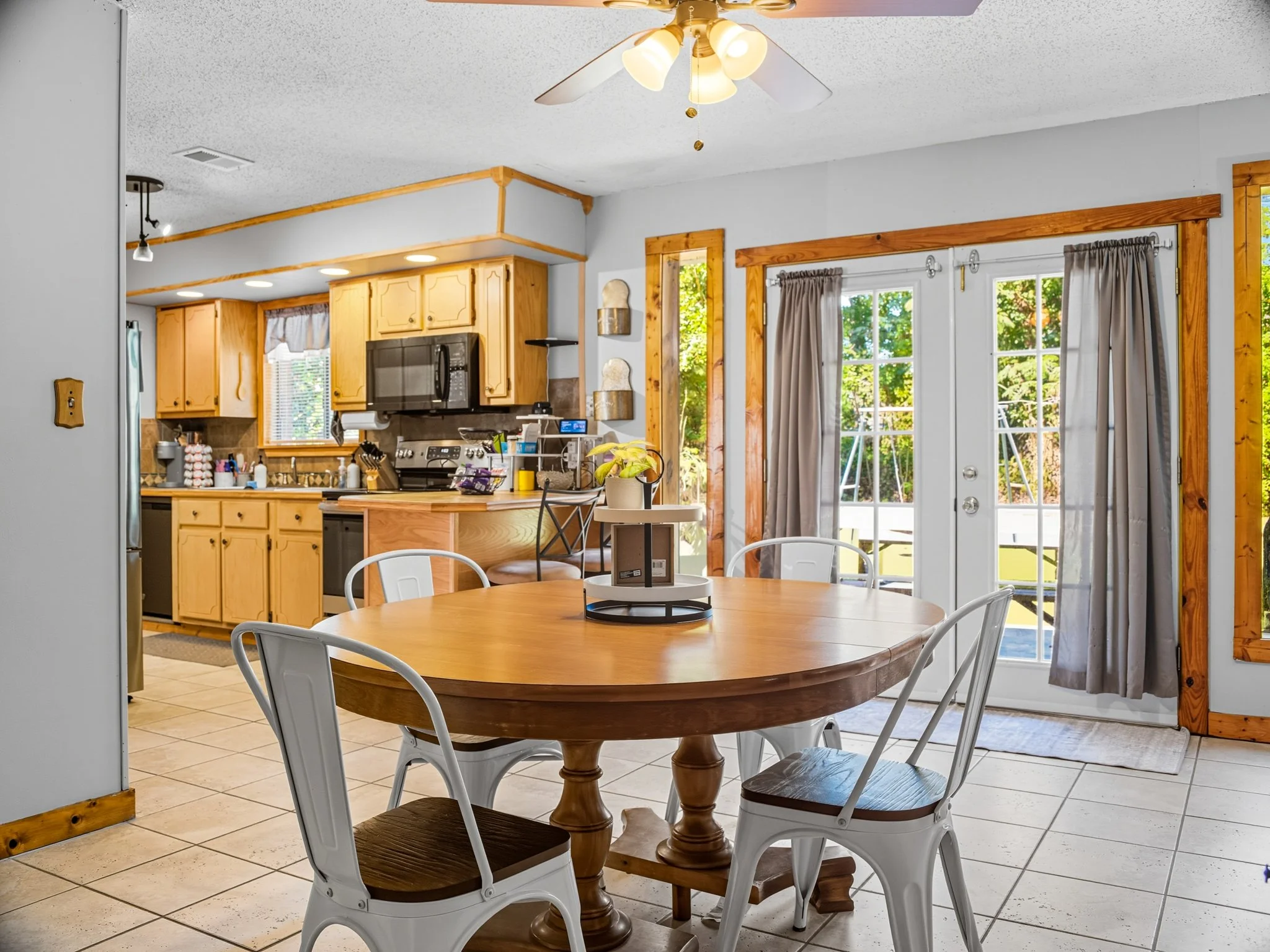 Bright kitchen with wooden cabinets, a dining table with four chairs, and glass doors leading outside with trees in view.