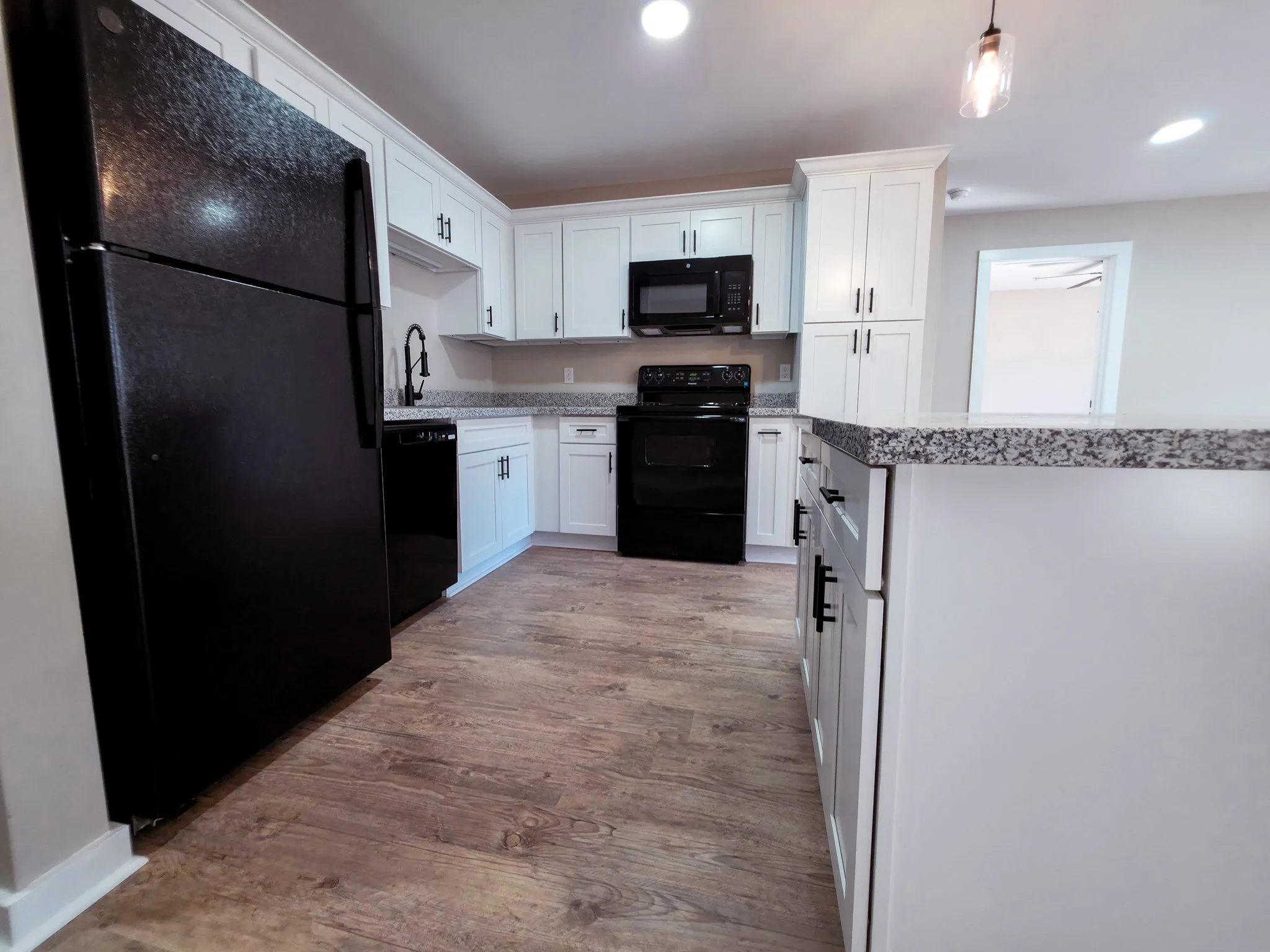Modern kitchen with black appliances, white cabinetry, granite countertops, hardwood floors, and a black stove in the center.