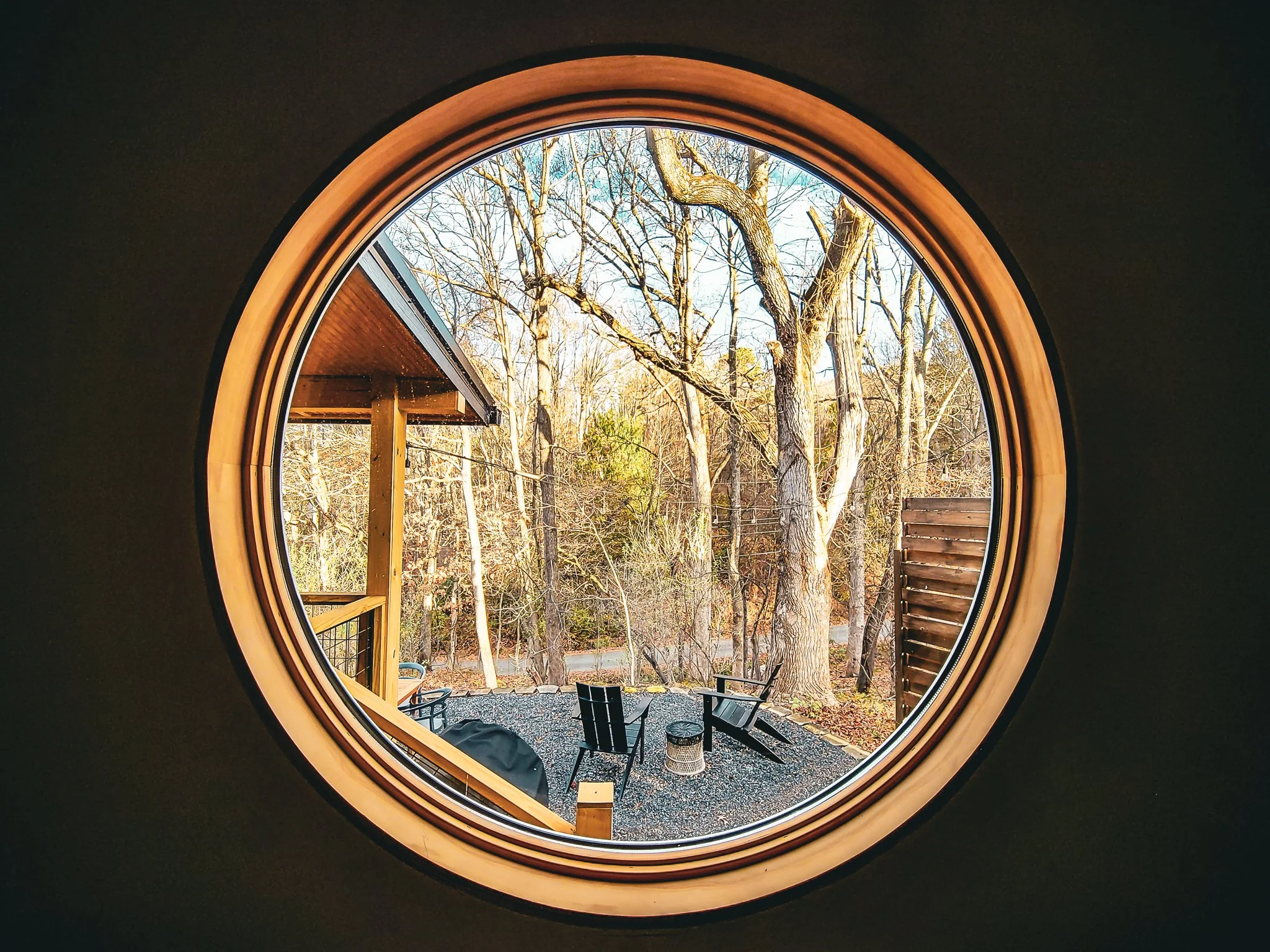 View of an outdoor patio with chairs and trees, seen through a round window.