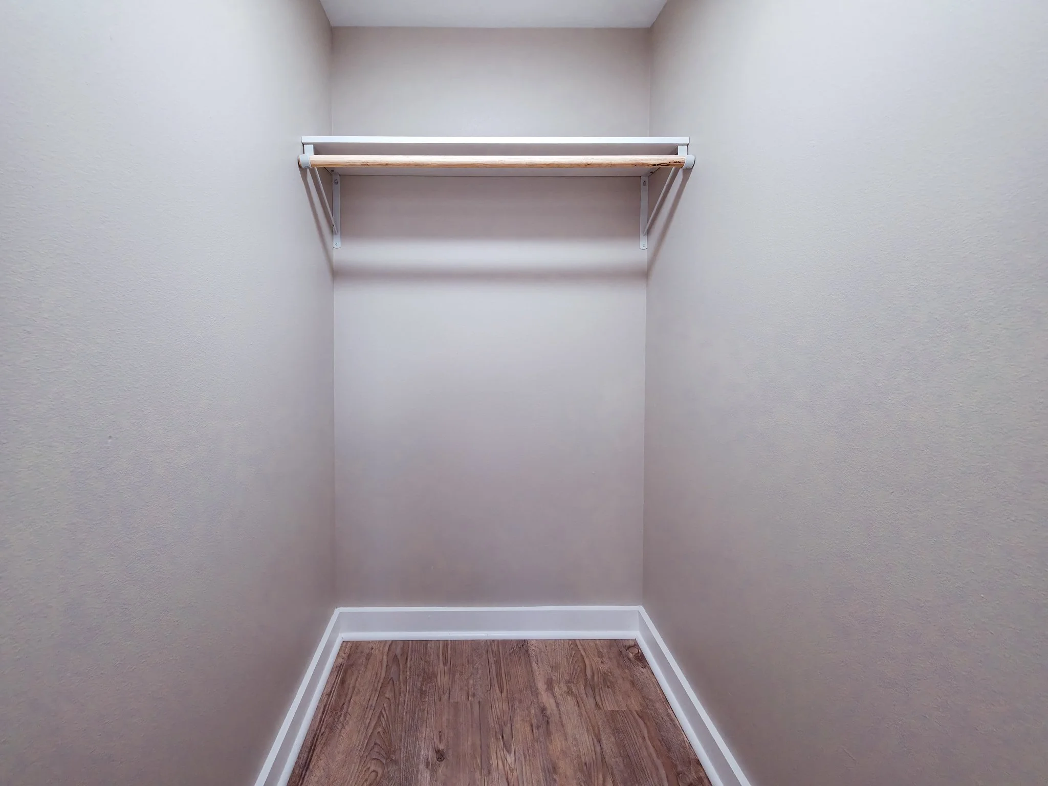 Empty walk-in closet with a single shelf and clothing rod, beige walls, and wooden floor.