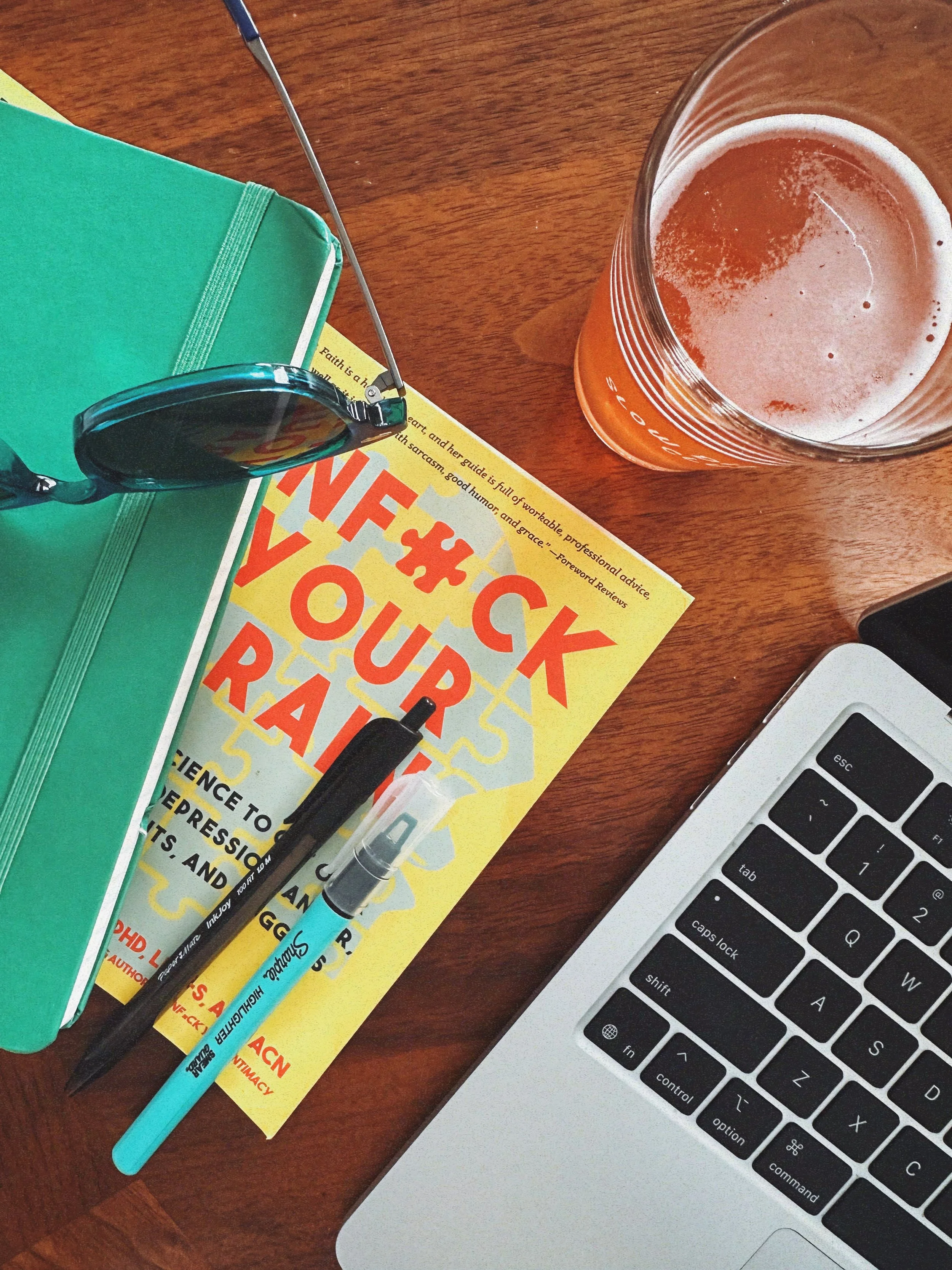 messy desk with unf*ck your brain book and macbook - ashley kesner