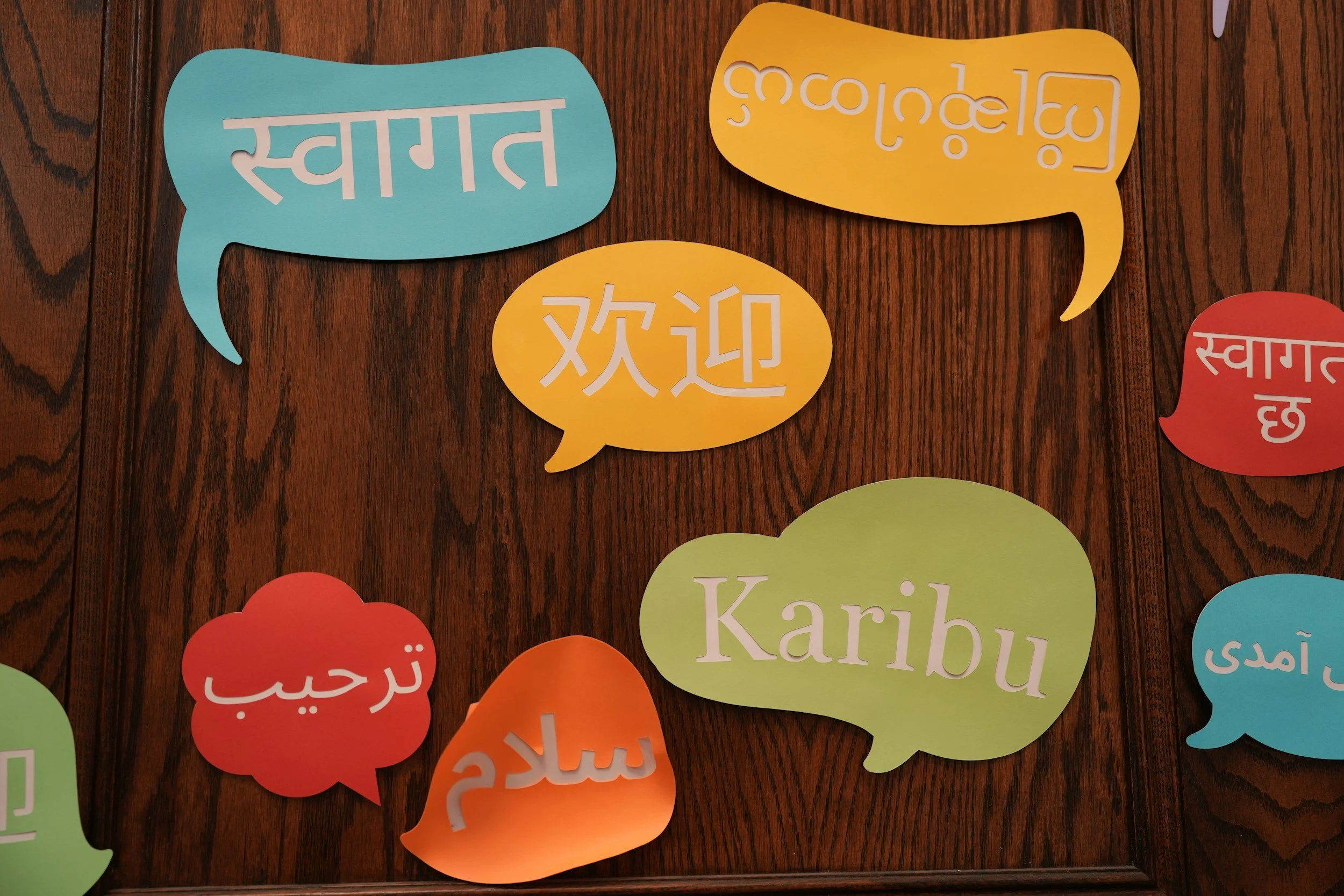 Dialogue bubbles in various languages cut out of colorful paper on a background of woodgrain.