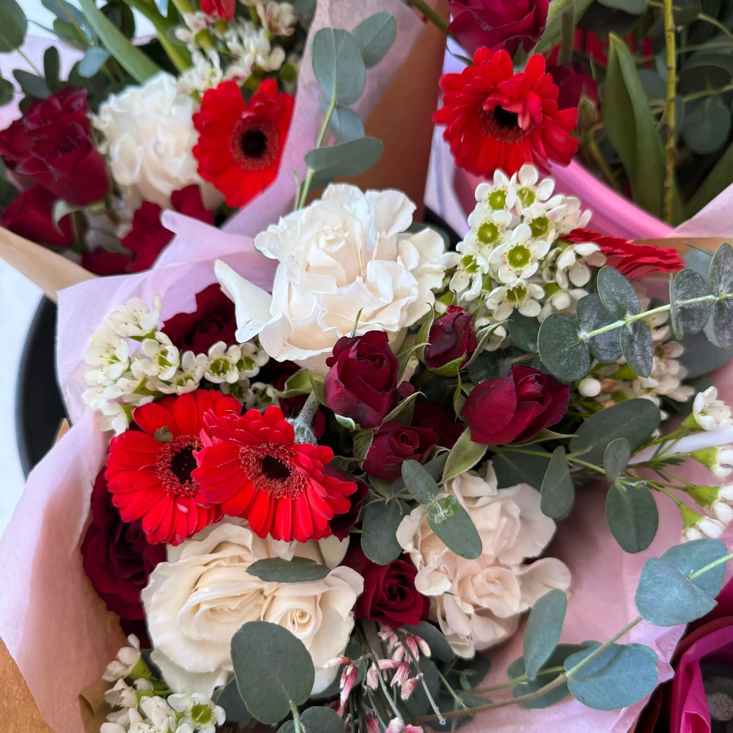 Bouquet of red, white, and cream flowers with green foliage wrapped in pink and brown paper.