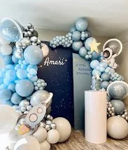 Decorative balloon arch with blue, white, and silver balloons surrounding a dark blue backdrop with the name 'Amari' in white script.