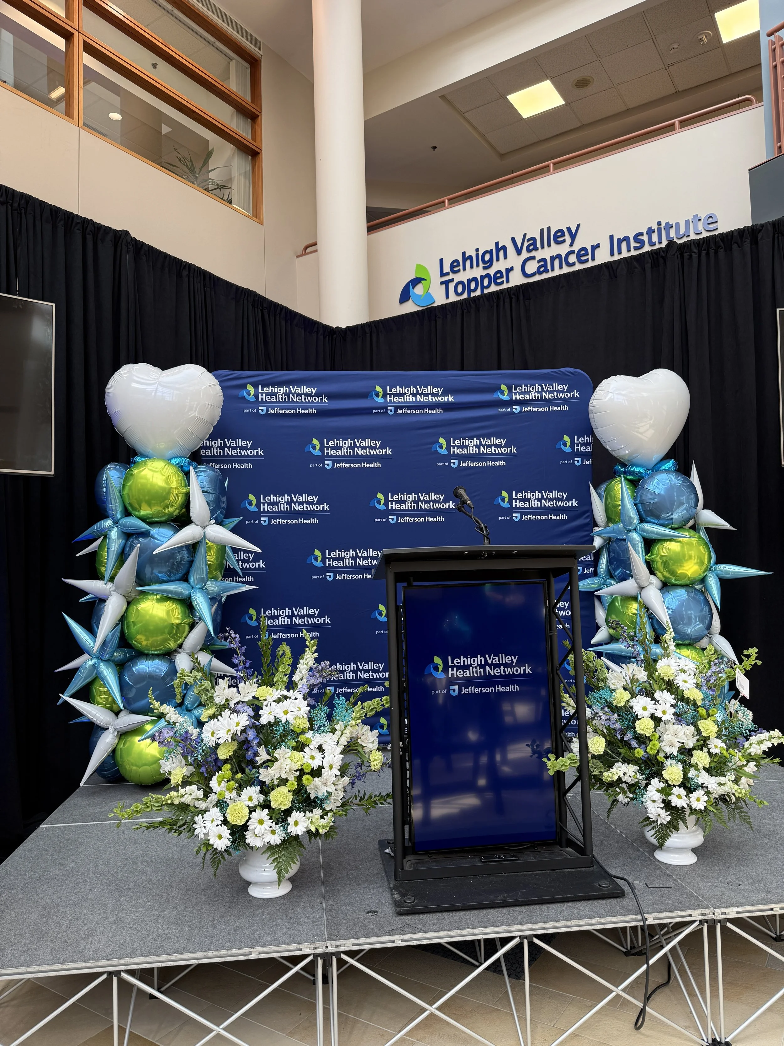 Stage setup with balloons and floral arrangements at Lehigh Valley Topper Cancer Institute, part of Lehigh Valley Health Network and Jefferson Health.