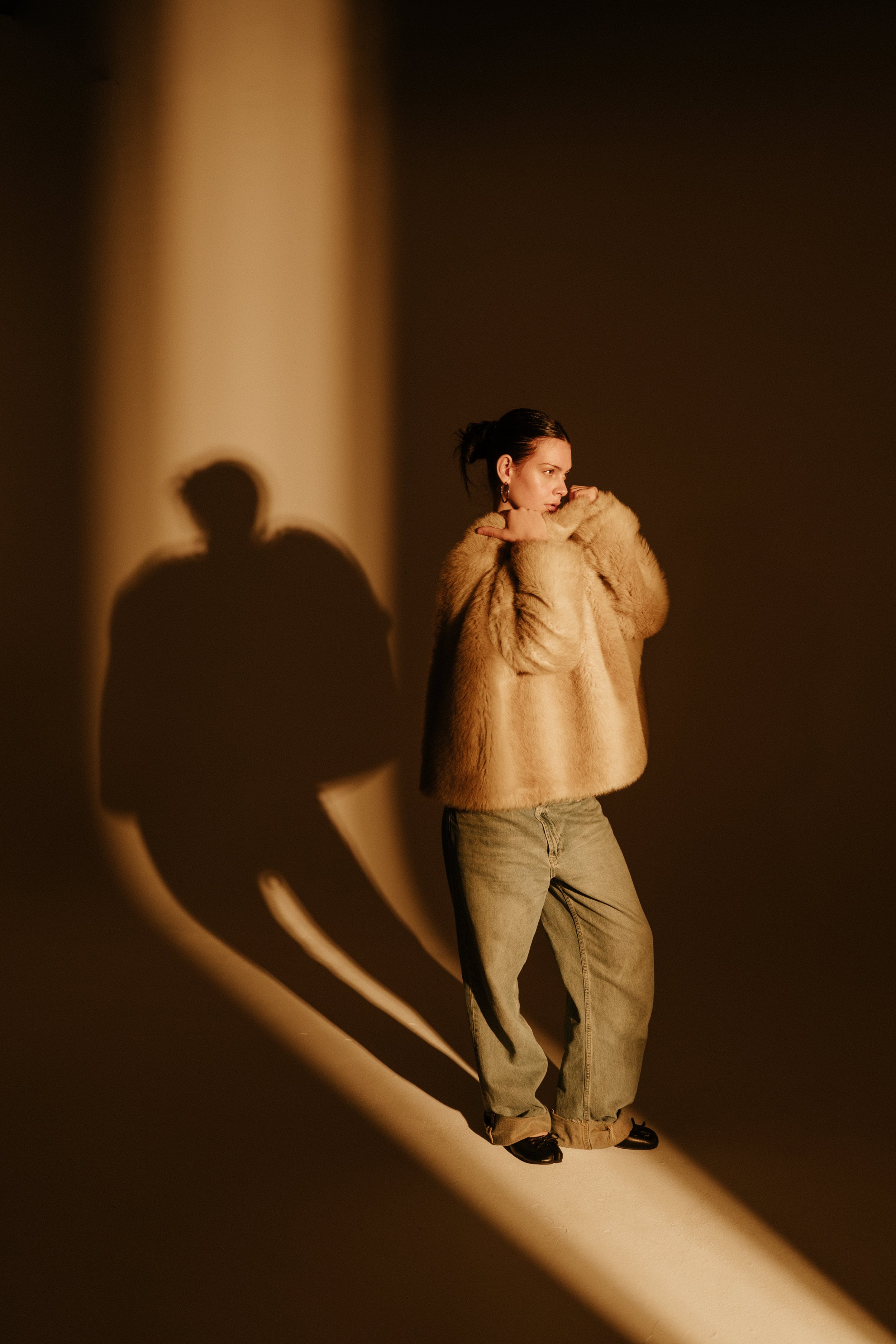 Person wearing a fur coat and jeans, standing in dramatic lighting with a prominent shadow.