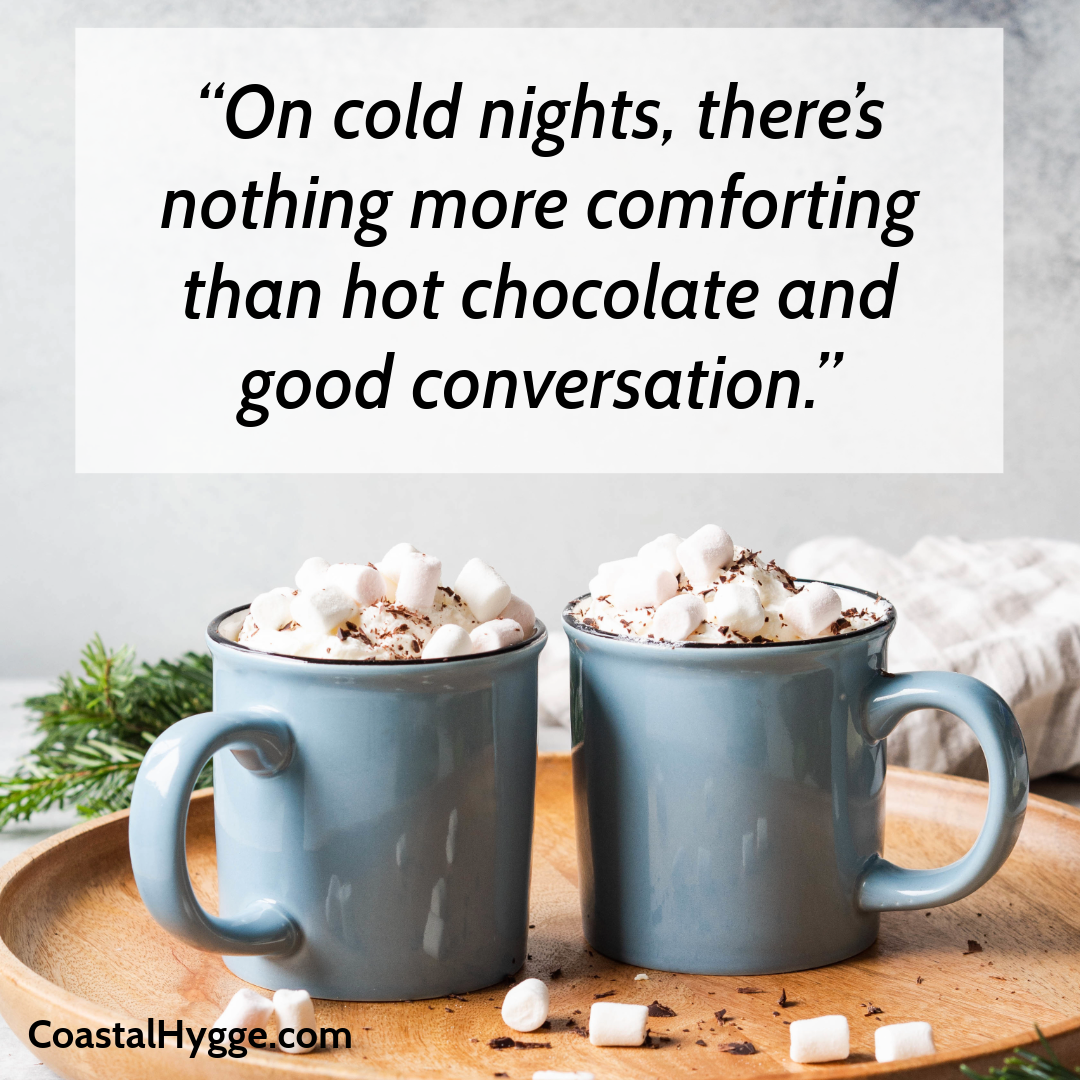 A couple of light blue cups of hot chocolate topped with marshmallows and shaved chocolate sitting on a wooden tray.  The quote said "On cold nights, there's nothing more comforting than hot chocolate and good conversation."