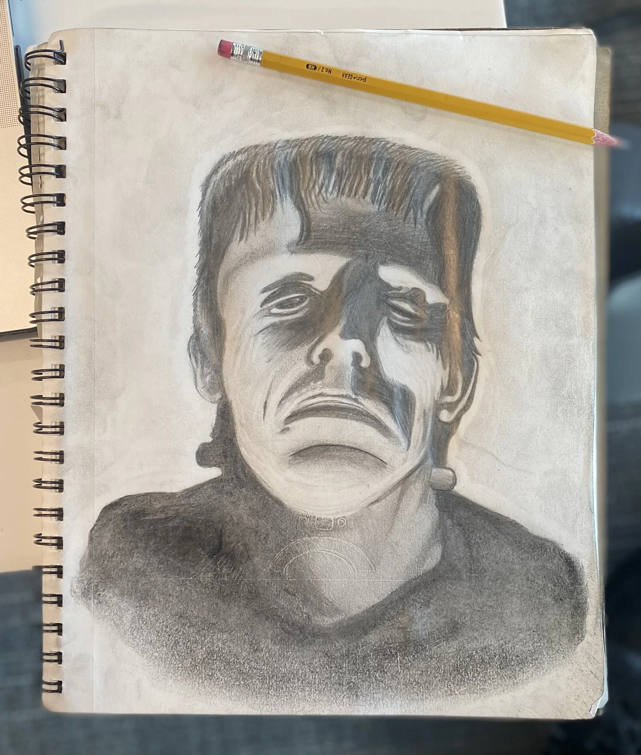 Black and white sketch of Frankenstein's monster on a notebook page with a yellow pencil resting on top.