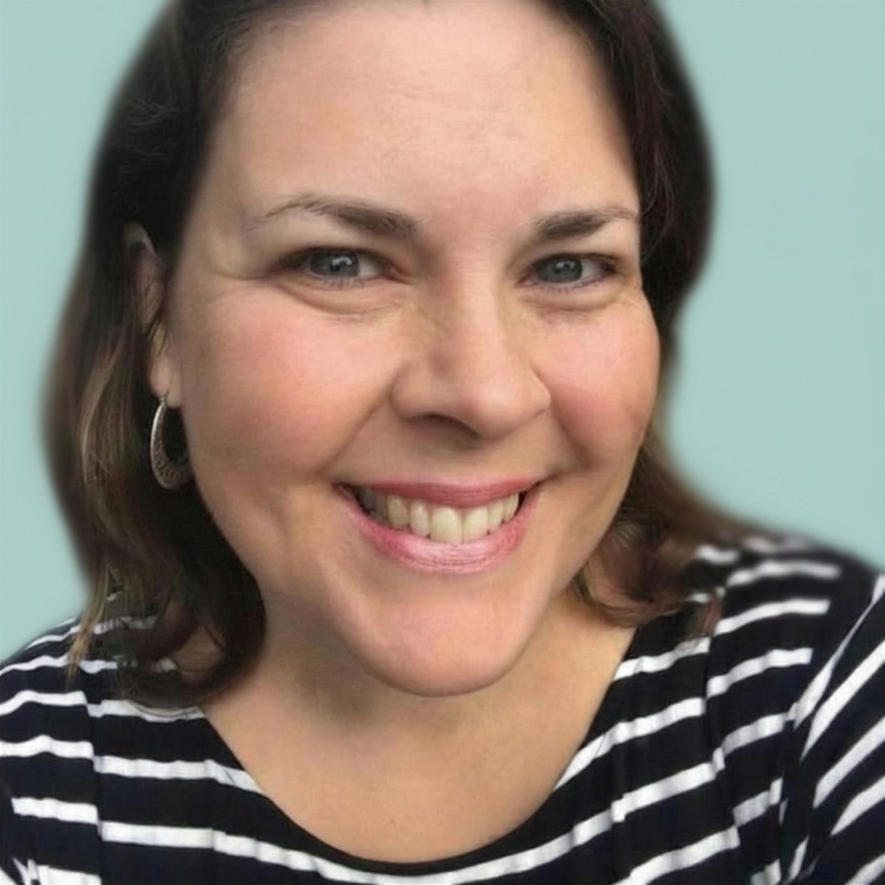 Close-up of a woman with shoulder-length brown hair, wearing a striped black and white shirt, smiling, with earrings and light makeup, against a light-colored background.