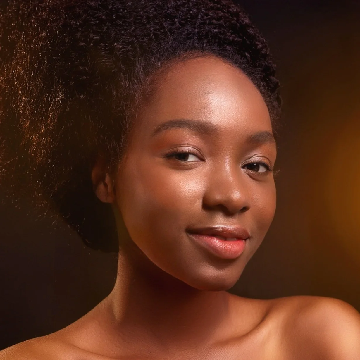 Close-up portrait of a young Black woman with natural curly hair & stunning, dewy skin.