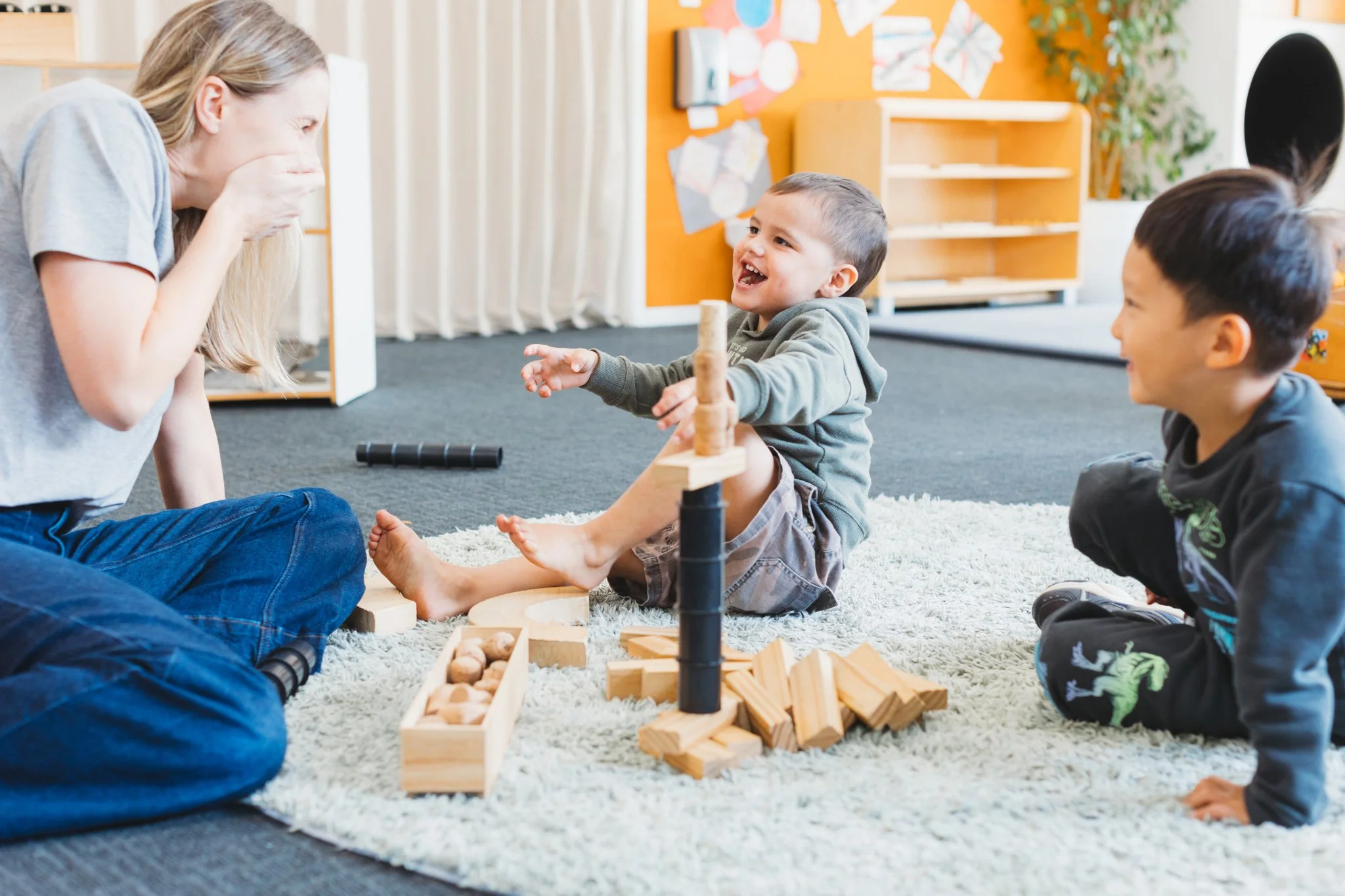 Qualified ECE teacher and two boys playing with wooden blocks on a rug at Auckland childcare near Onehunga